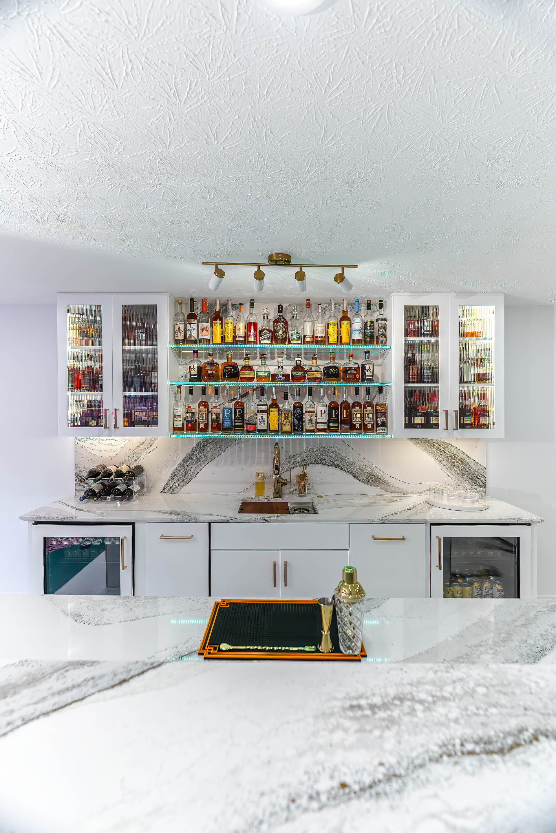 A home bar with white cabinets, liquor bottles, and a marble countertop.
