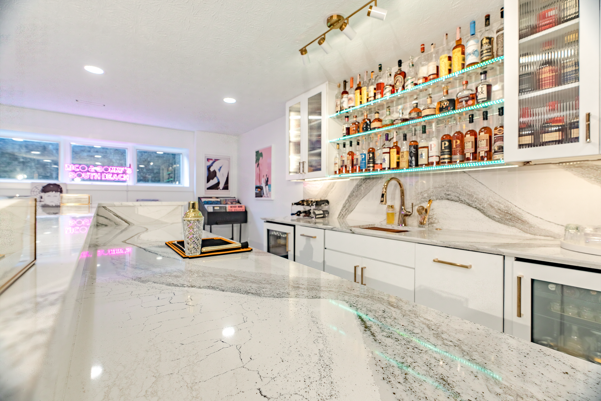 A modern home bar with white cabinets, marble countertops, and a well-stocked liquor display.