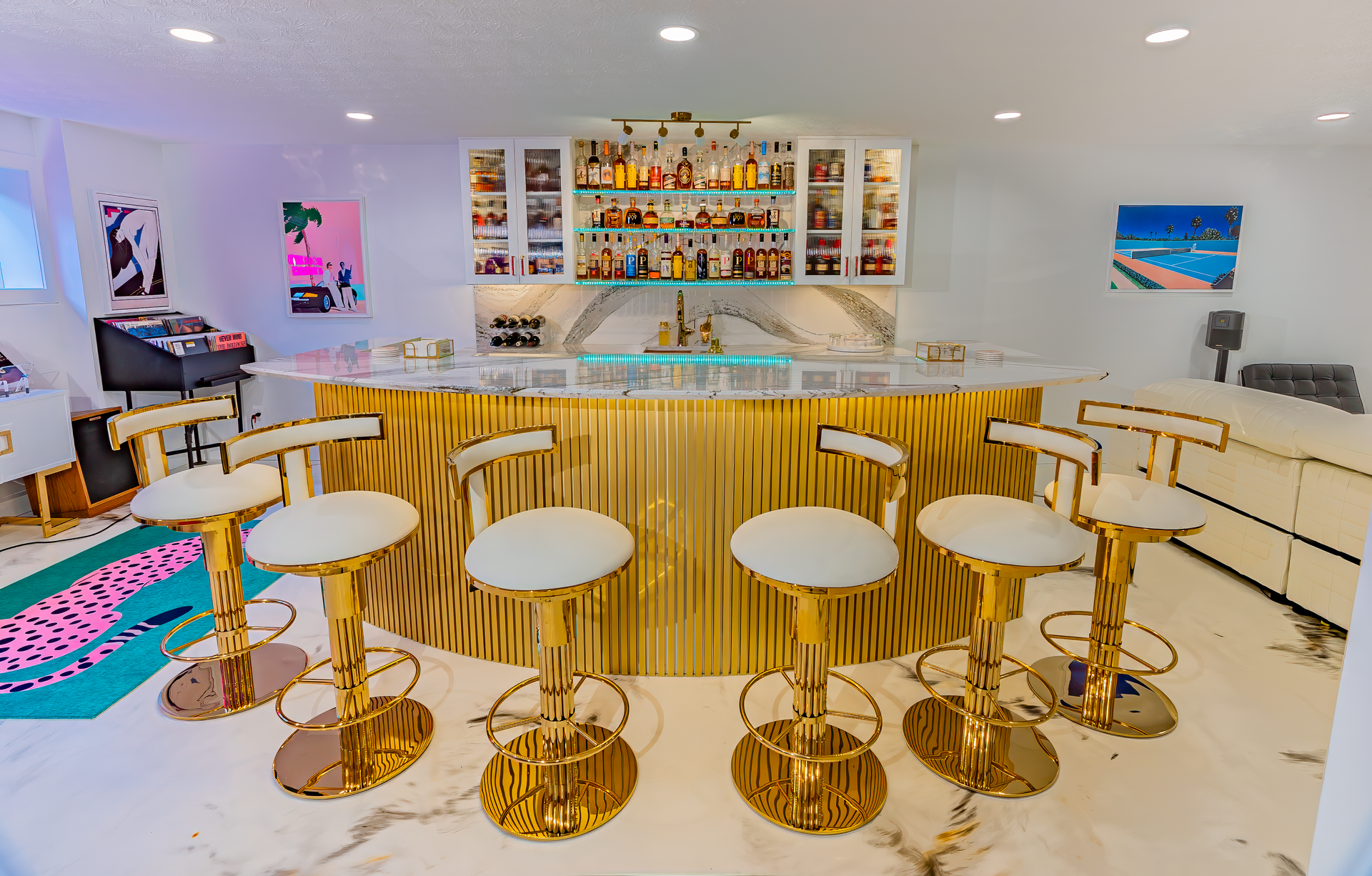 A luxurious home bar with gold accents, white leather stools, and a well-stocked liquor display.