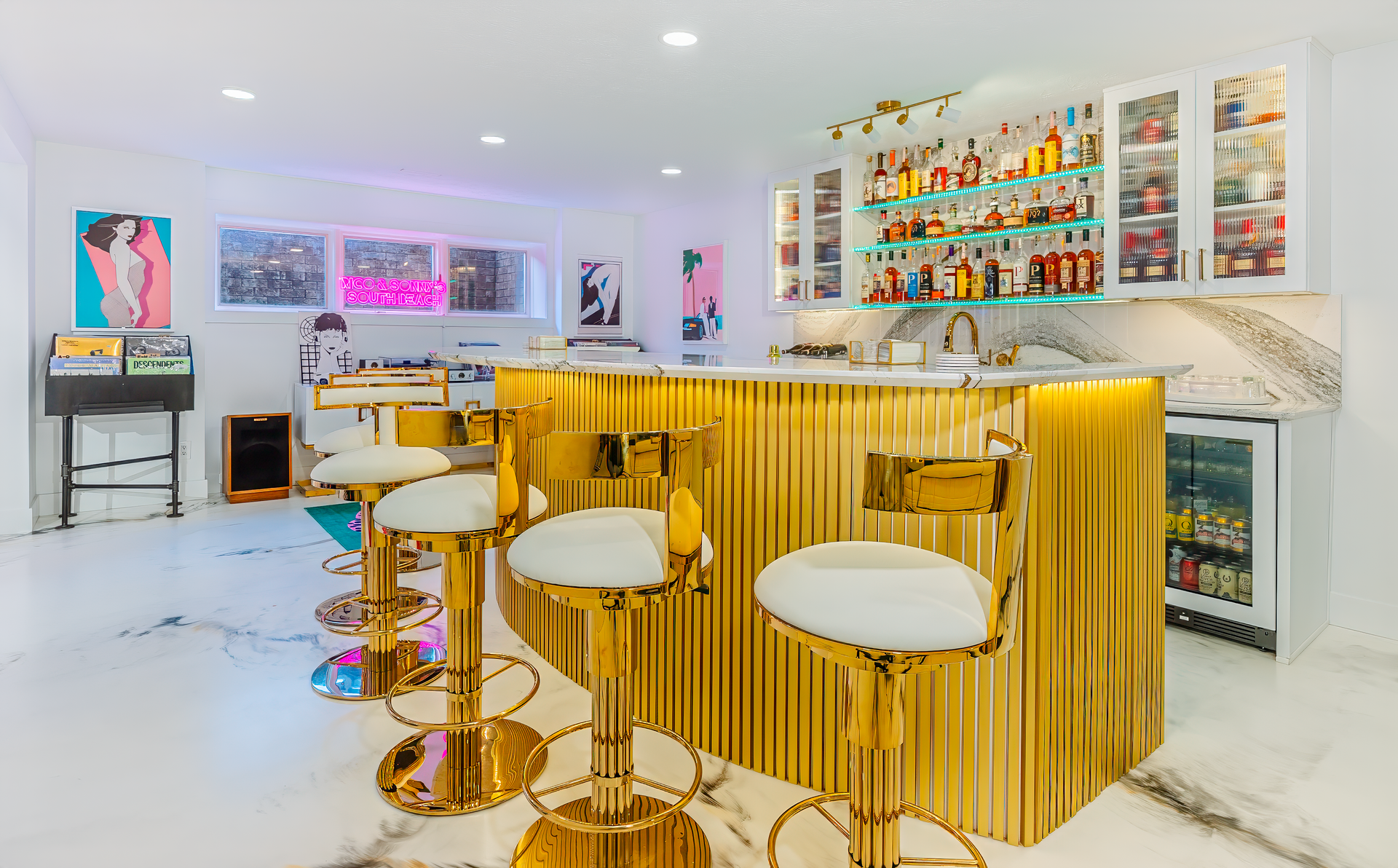 A glamorous gold and white home bar with stools, lit cabinets, and liquor bottles.
