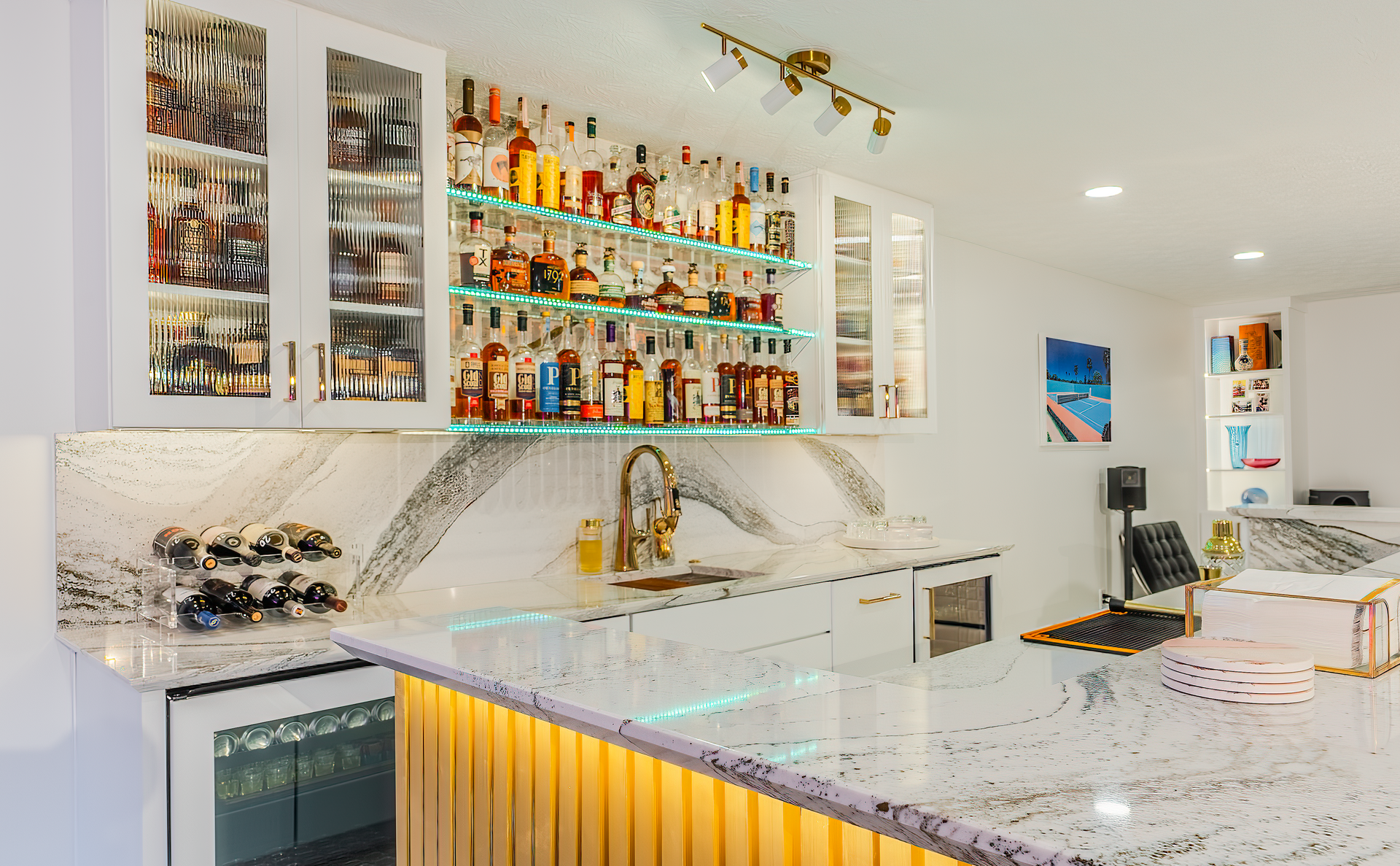 Basement bar with liquor bottles on shelves, marble counters, and gold accents.