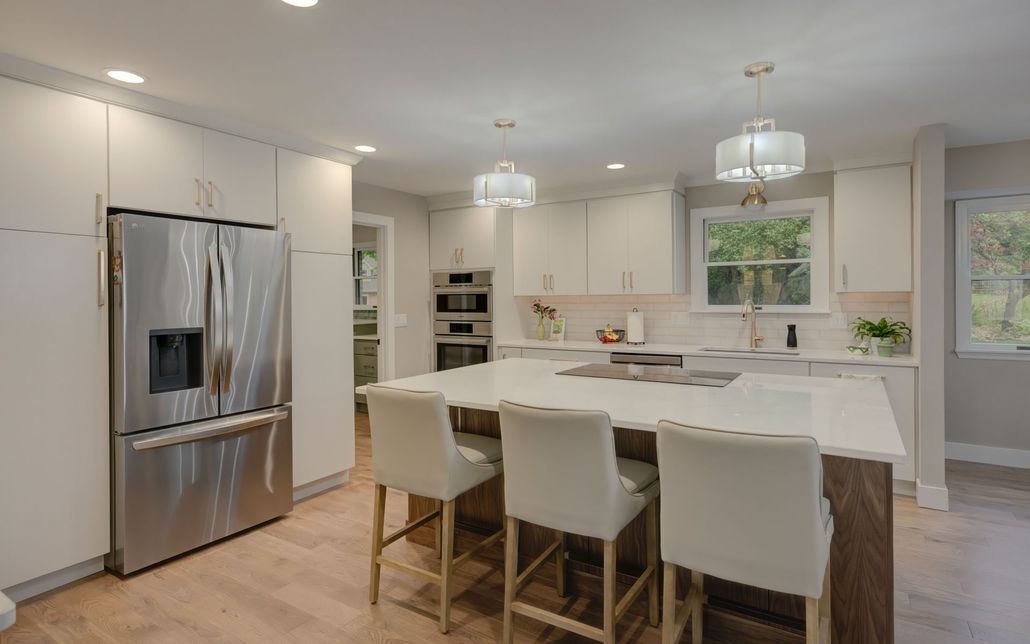 A kitchen with white cabinets, stainless steel appliances, a large island, and a refrigerator.