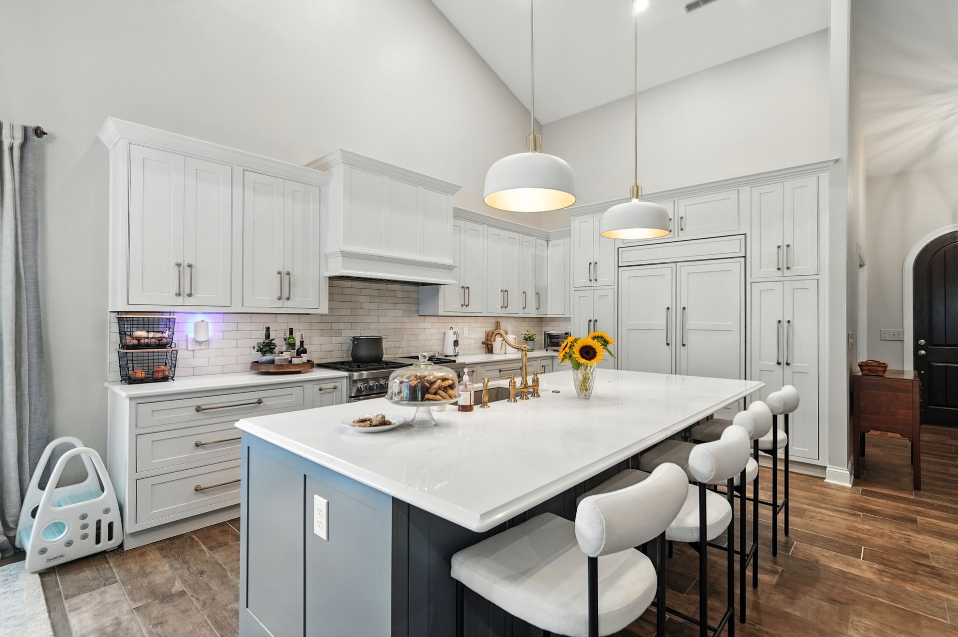 Modern kitchen with white cabinets, gray island, bar stools, and a sunflower.