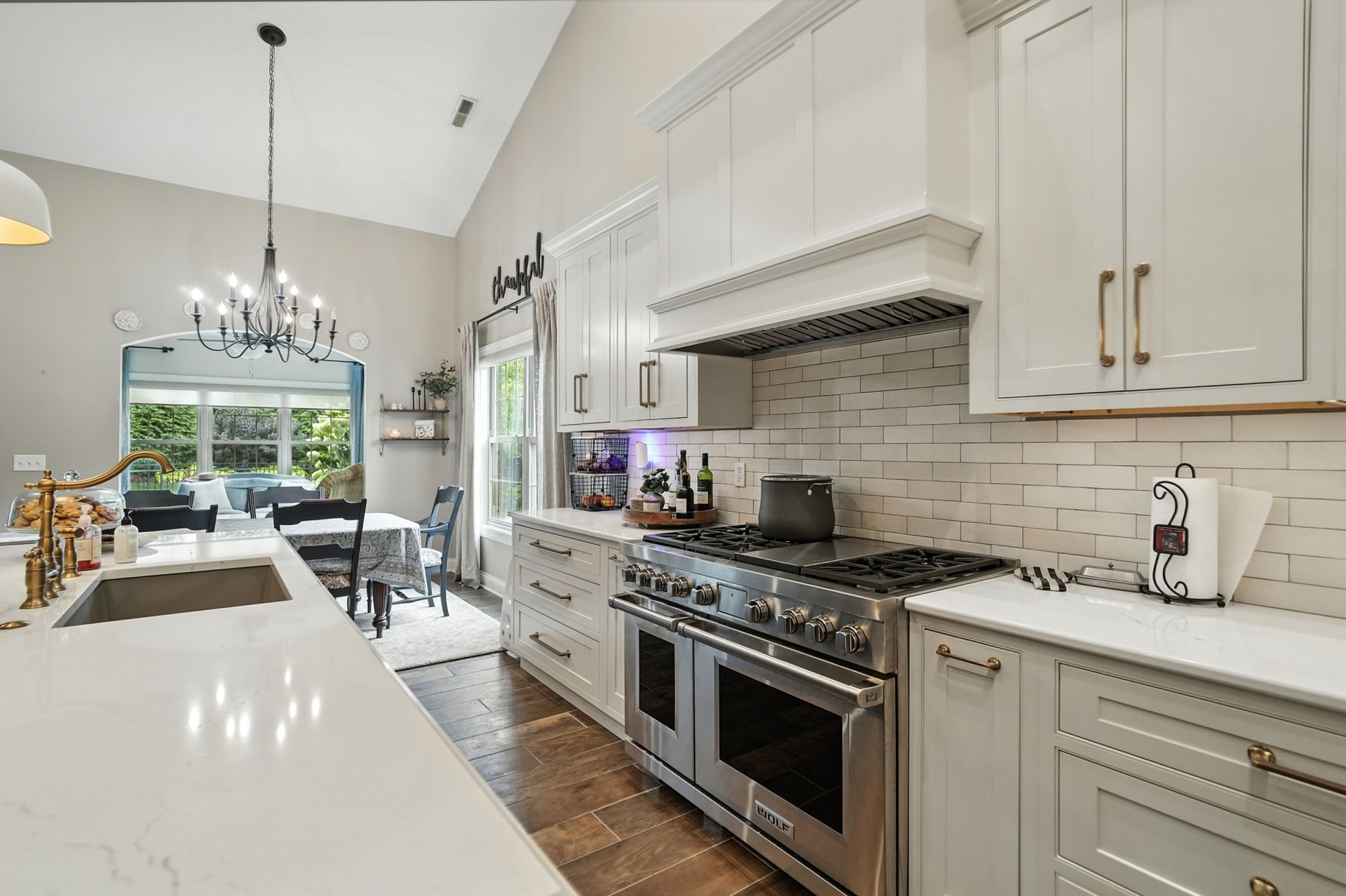 A modern kitchen with white cabinets, a stainless steel range, and a view of a dining area.