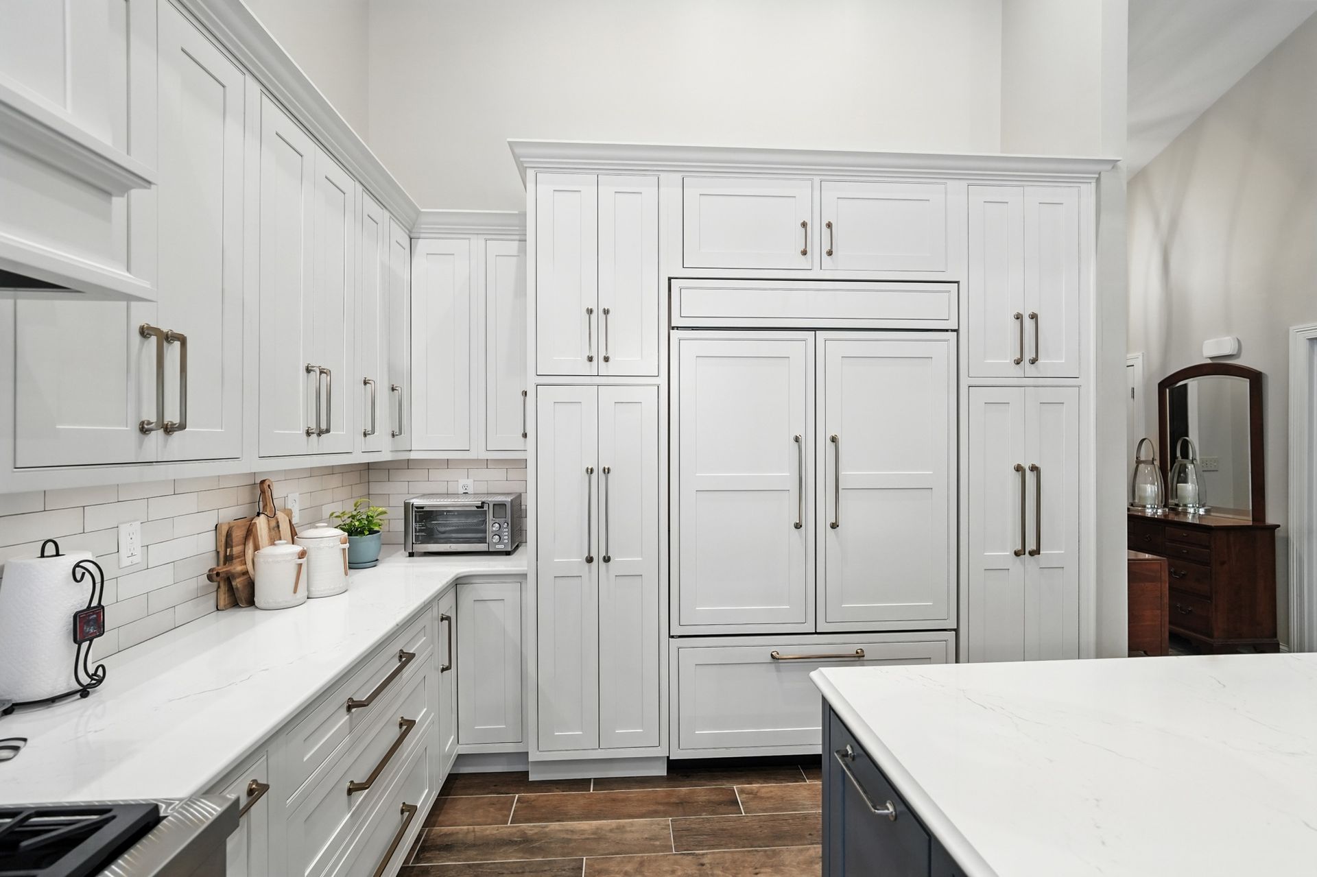 White kitchen with cabinets, countertop, refrigerator, and a dark-blue island, hardwood floor.