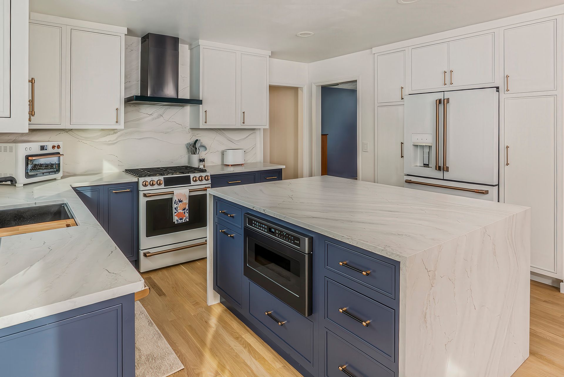 Modern kitchen with white upper cabinets, blue lower cabinets, and a marble island.