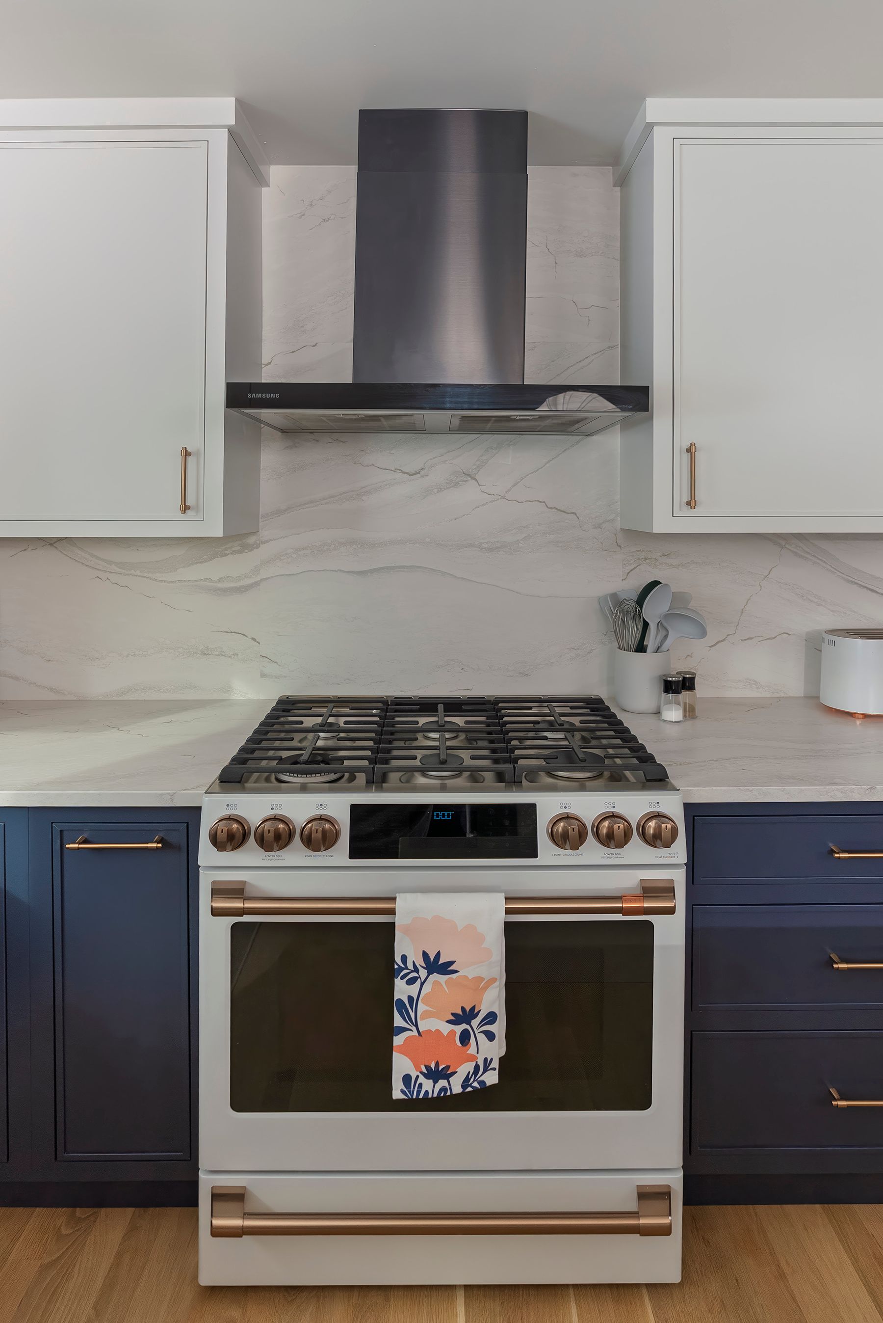 Kitchen with white and navy cabinets, stainless steel range hood, and stove with copper accents.