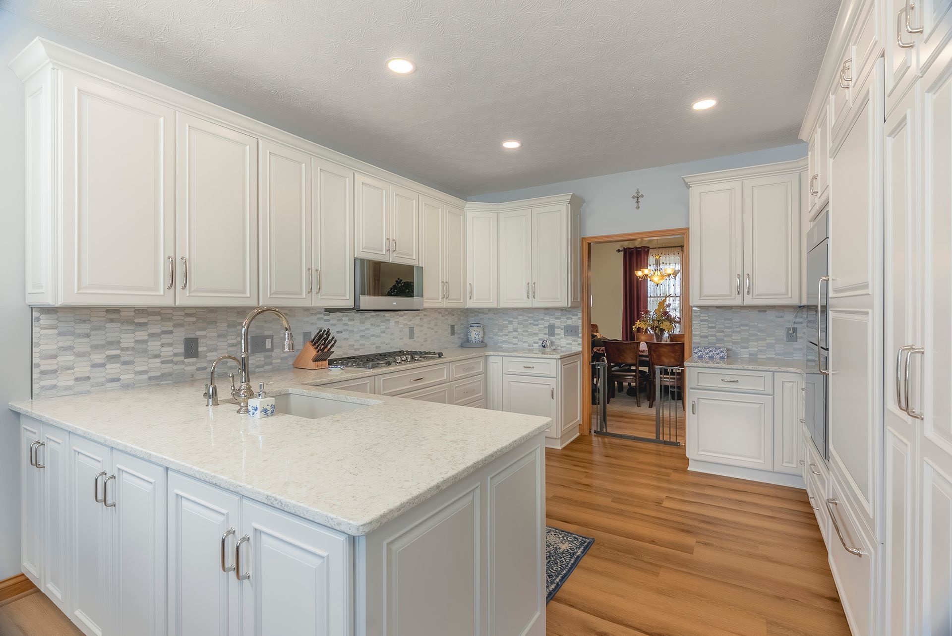 White kitchen with island, cabinets, and light-colored countertops; open doorway to dining room.