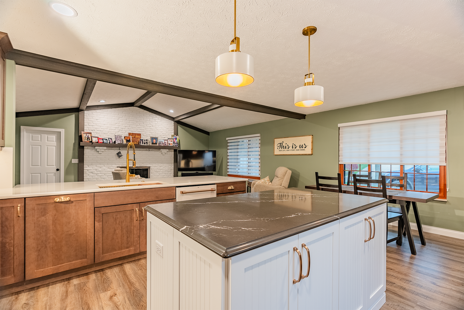Modern kitchen with island, wooden cabinets, pendant lights, and dining area with green walls.