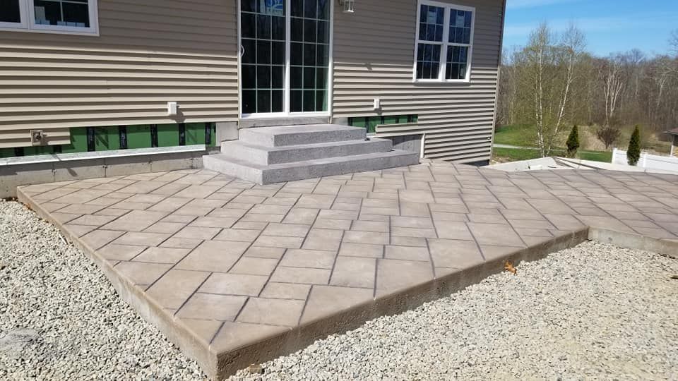 Gray paver patio with steps leading to sliding glass doors, surrounded by gravel.