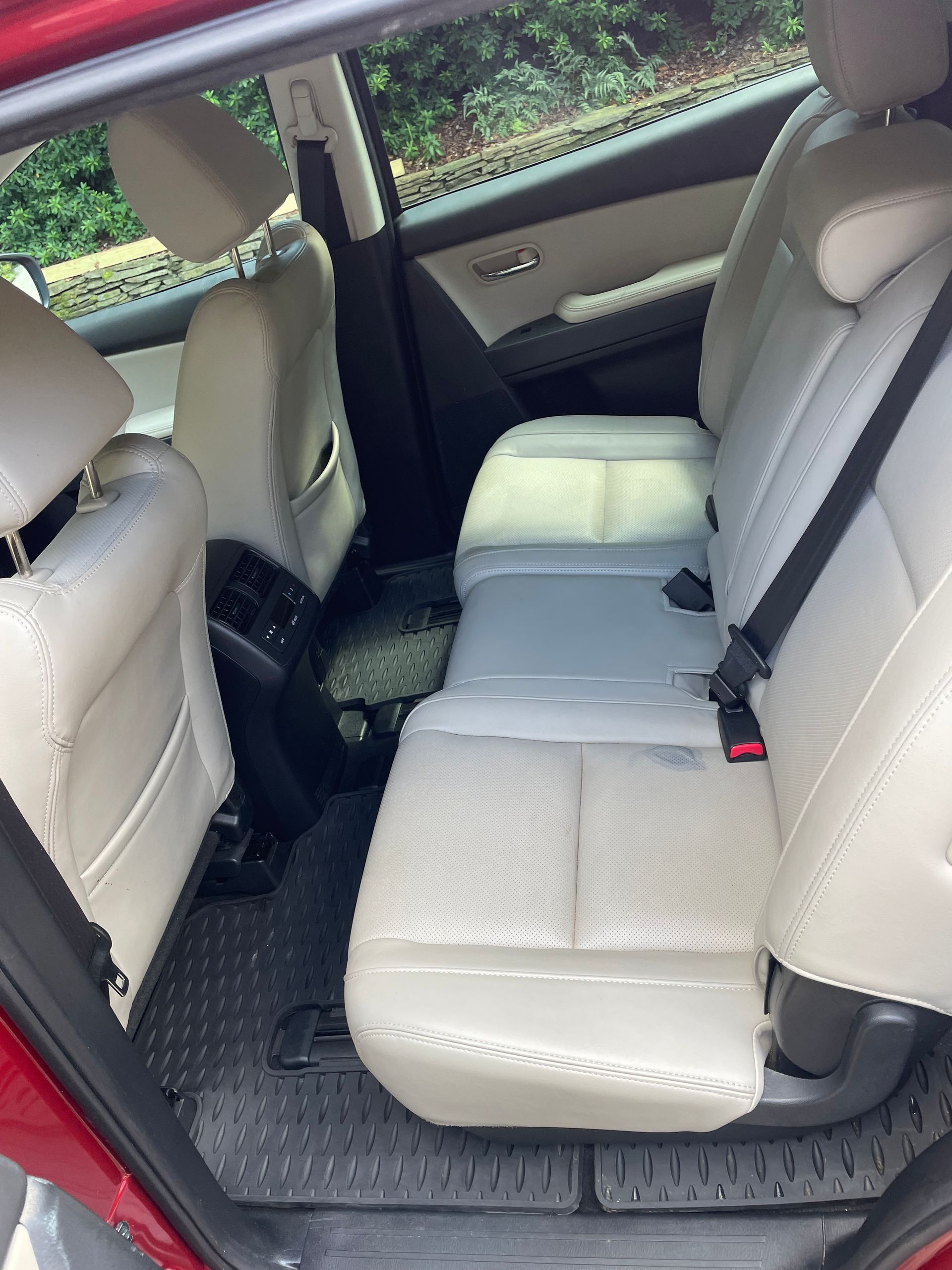 Backseat of a red car with tan leather seats and black floor mats.