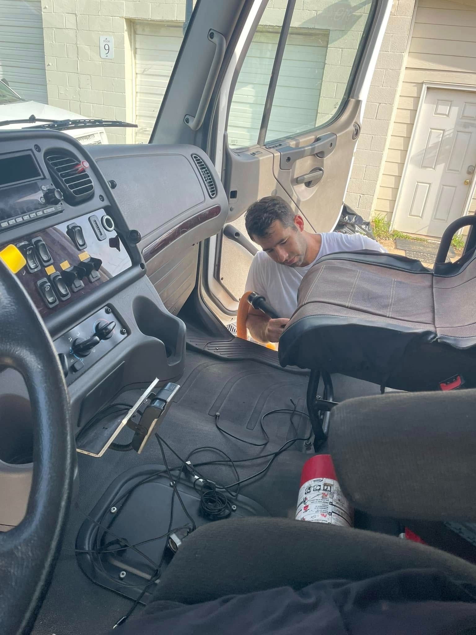 A man is inside a truck cab, working on the dashboard.