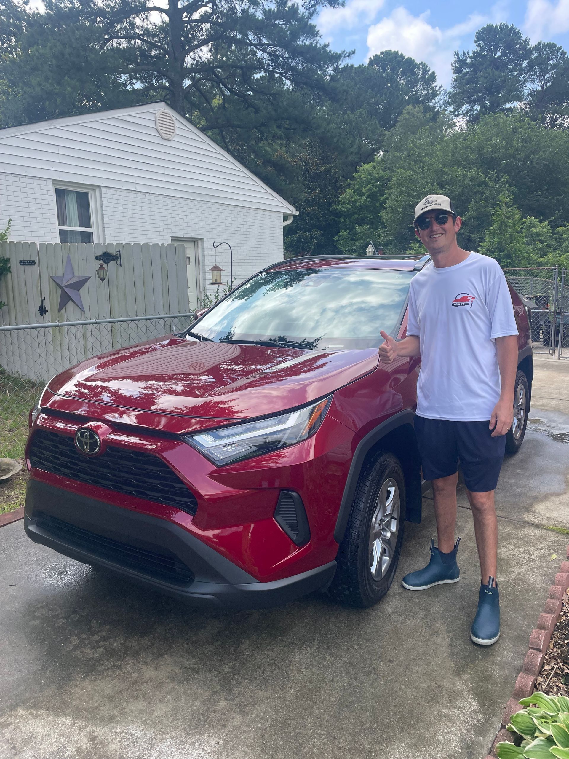 Man in sunglasses and t-shirt smiles next to a red Toyota SUV in front of a house.