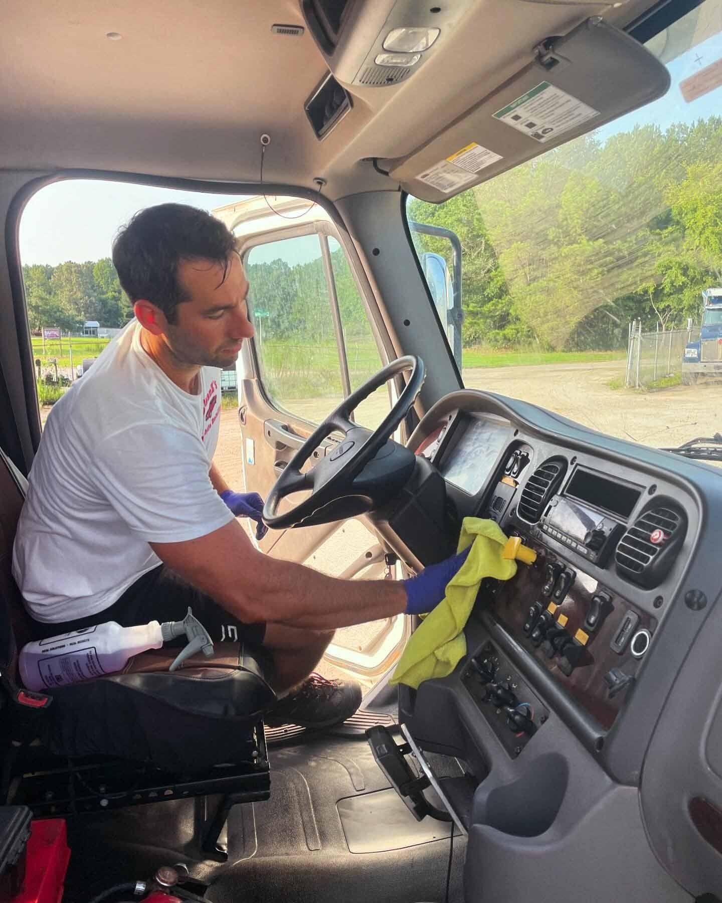 Man wearing gloves cleaning a truck dashboard with a yellow cloth. Inside the truck, outside view.