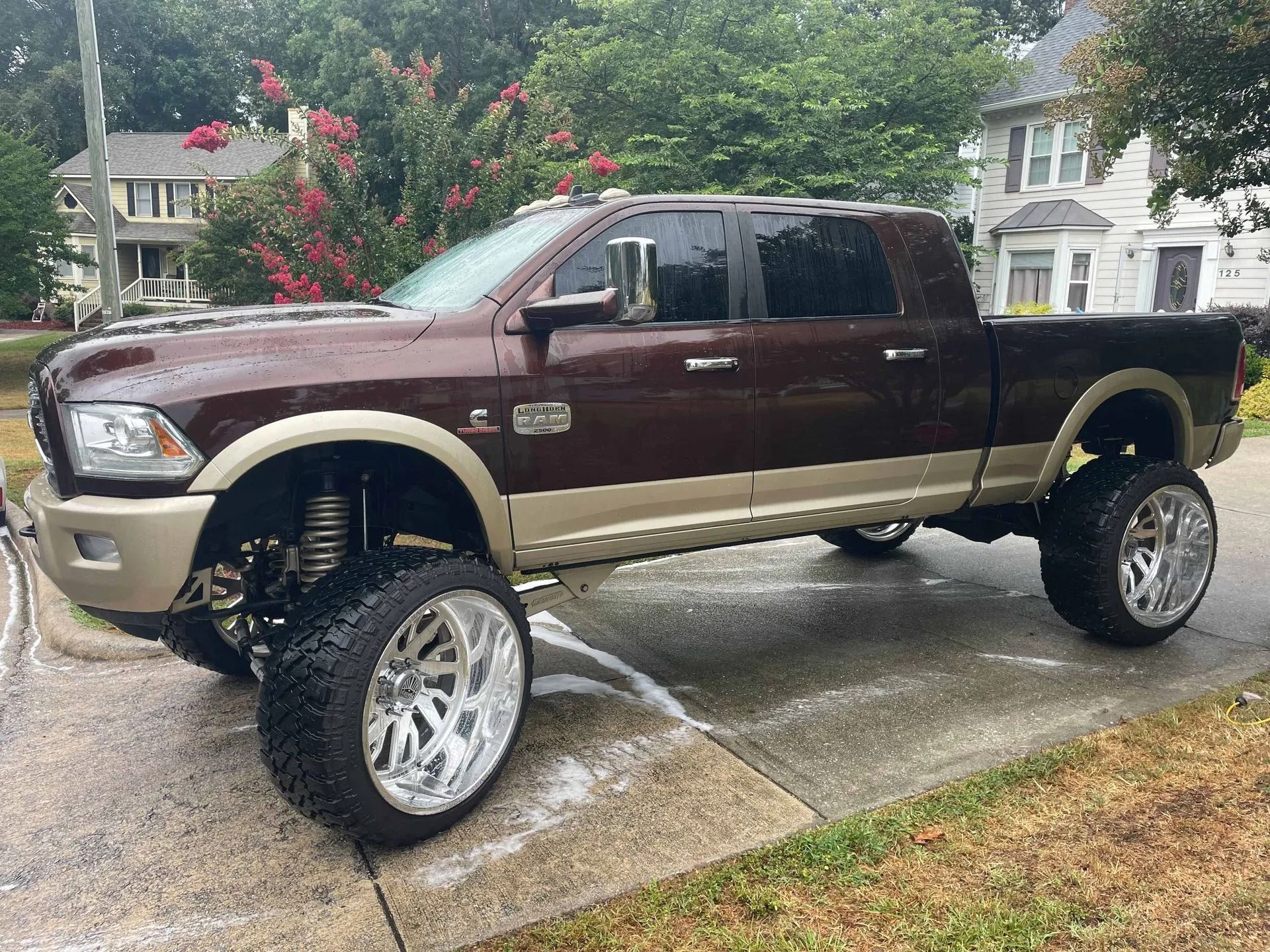 Brown and tan lifted Ram truck parked on a wet driveway. Shiny chrome wheels and tires.