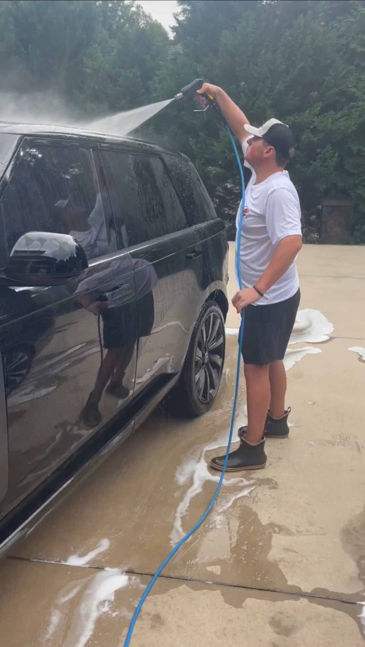 Man washing a black SUV with a hose, outdoors.