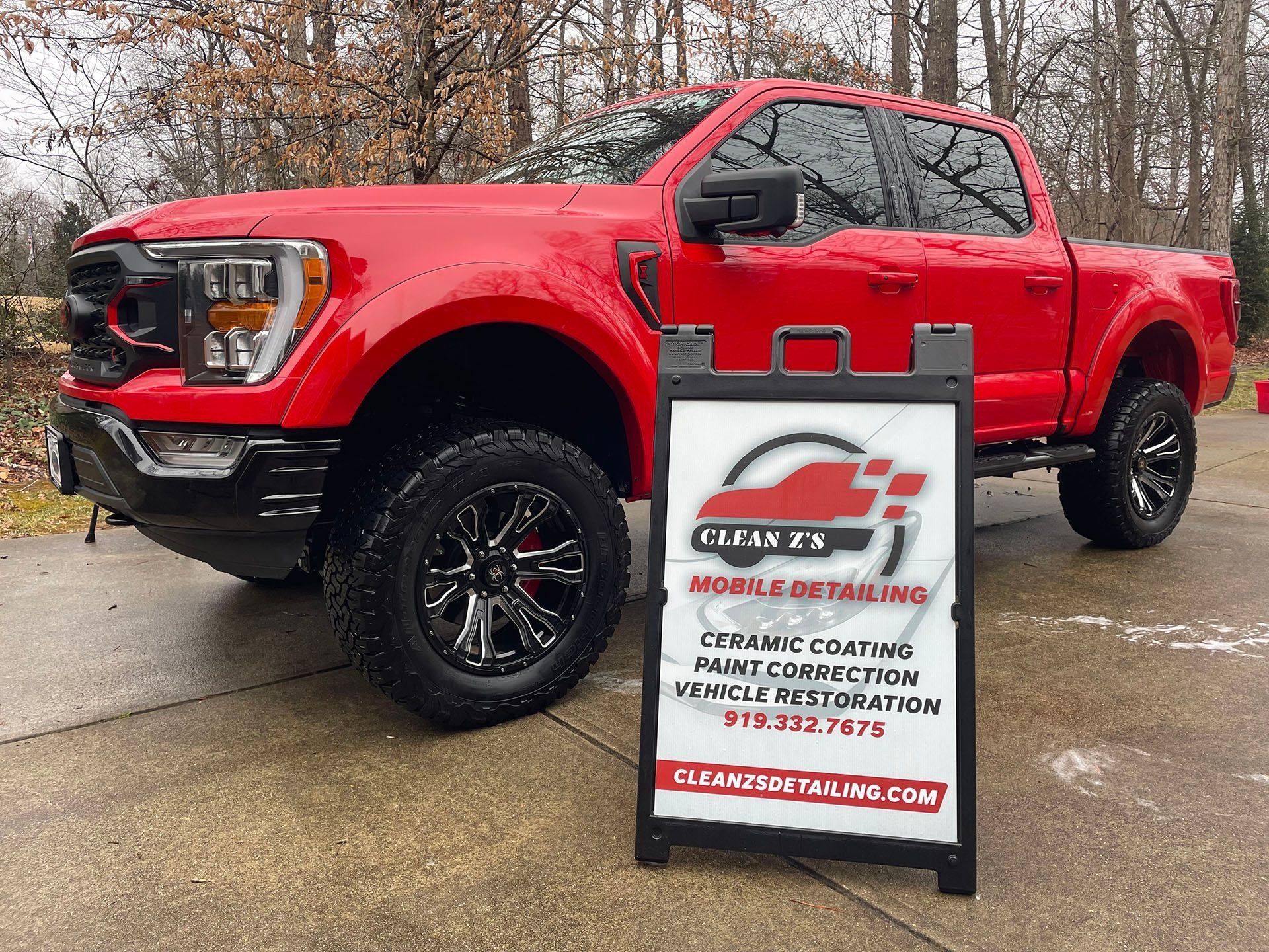 Red truck next to a detailing service sign. Ceramic coating, paint correction, and restoration.