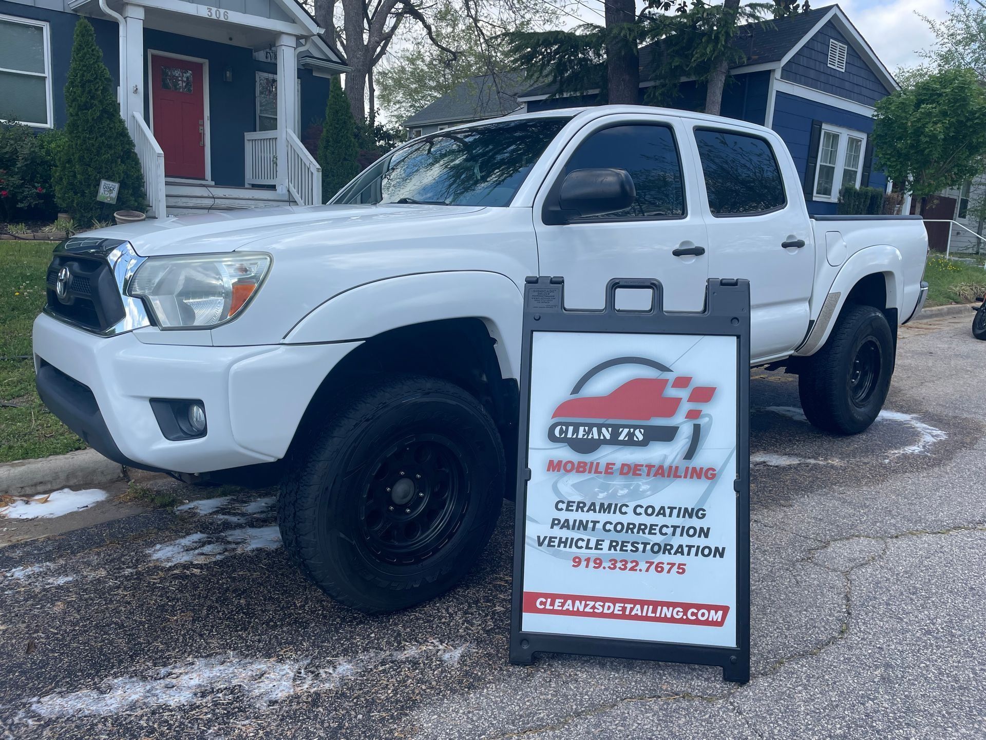 White truck parked on a street next to a sign advertising mobile car detailing services.