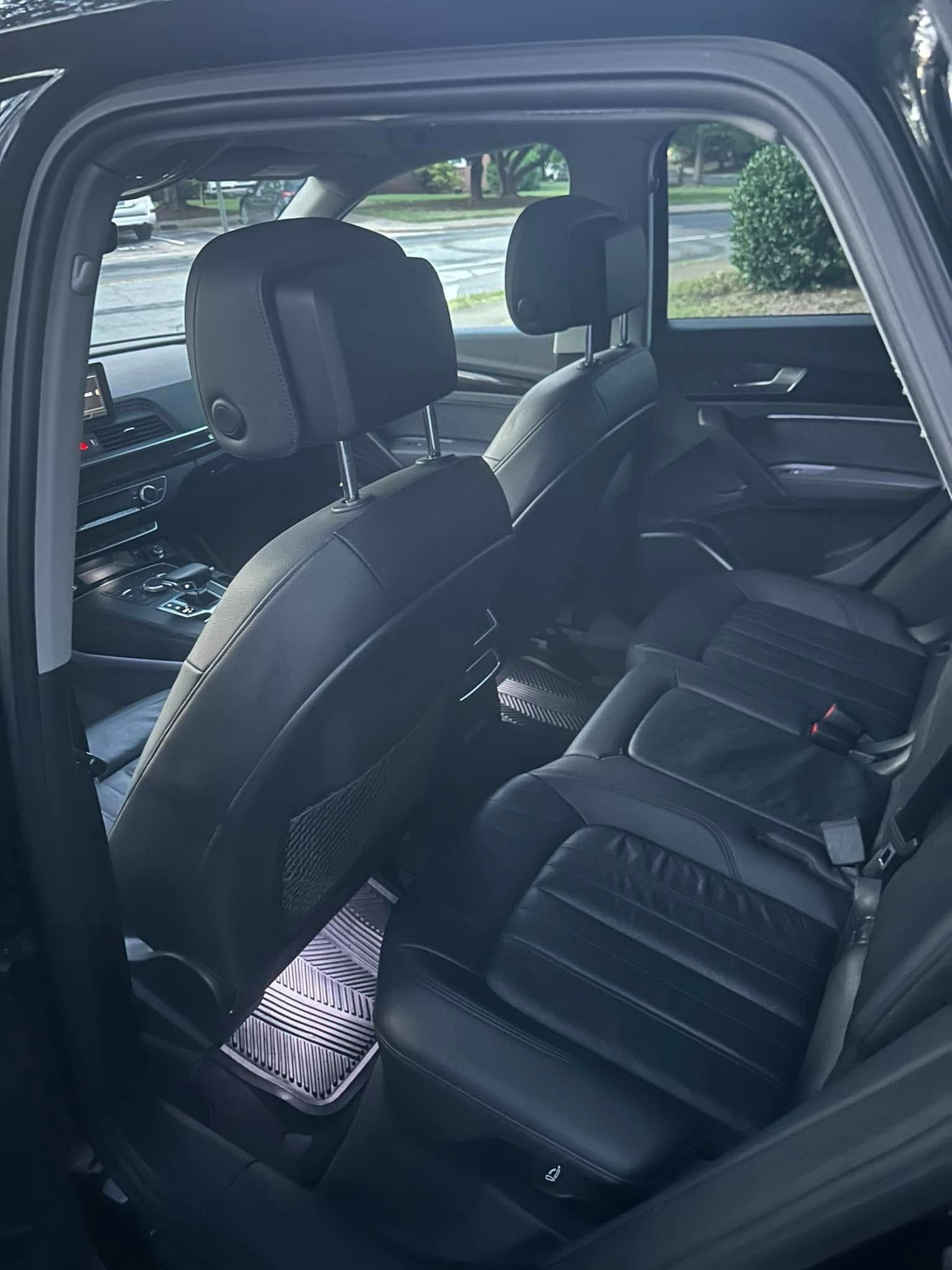 Black car interior with rear leather seats and headrests, including a black floor mat.