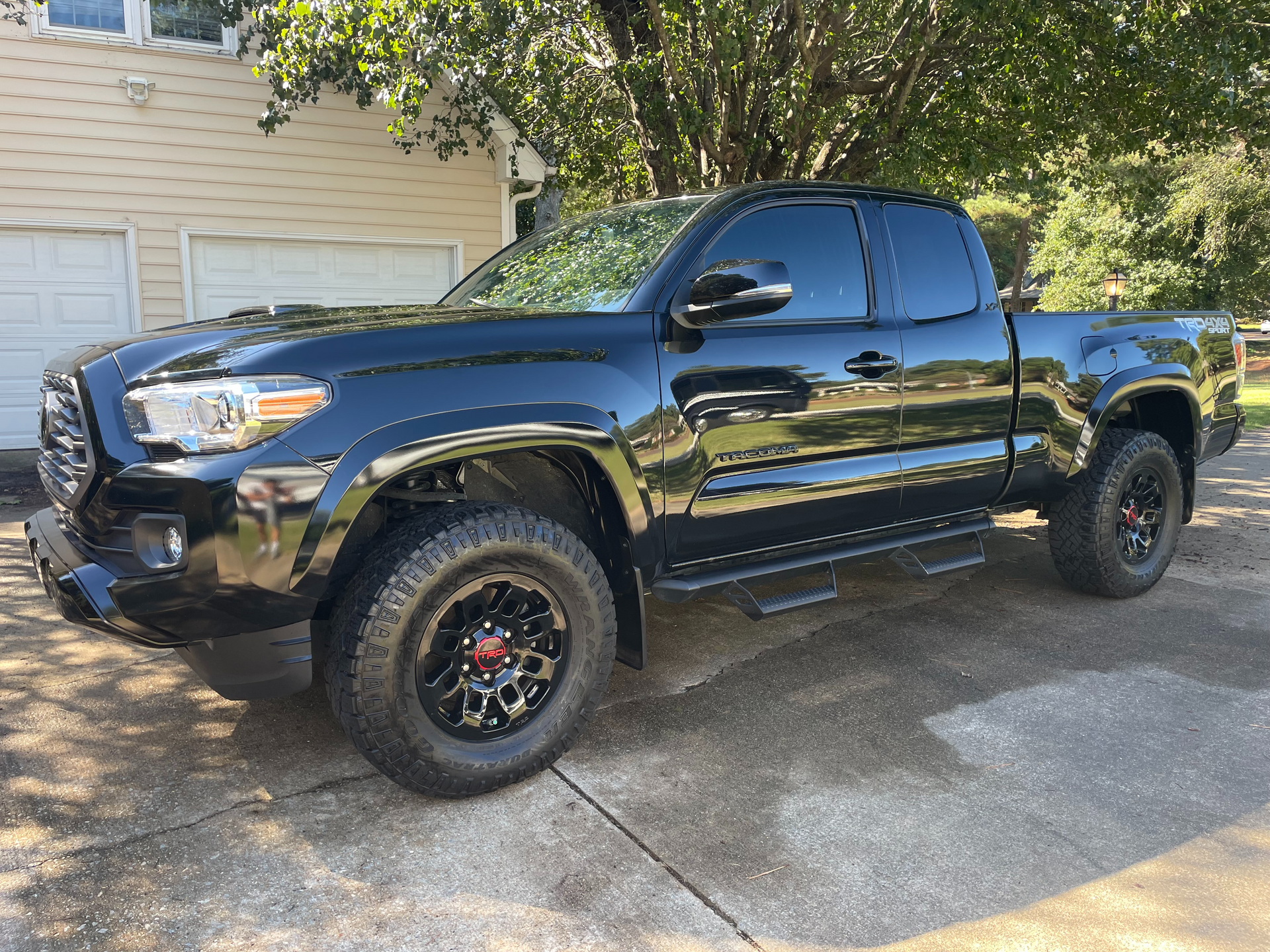 Black Toyota Tacoma truck parked outside a light-colored building, with dark tinted windows and black rims.