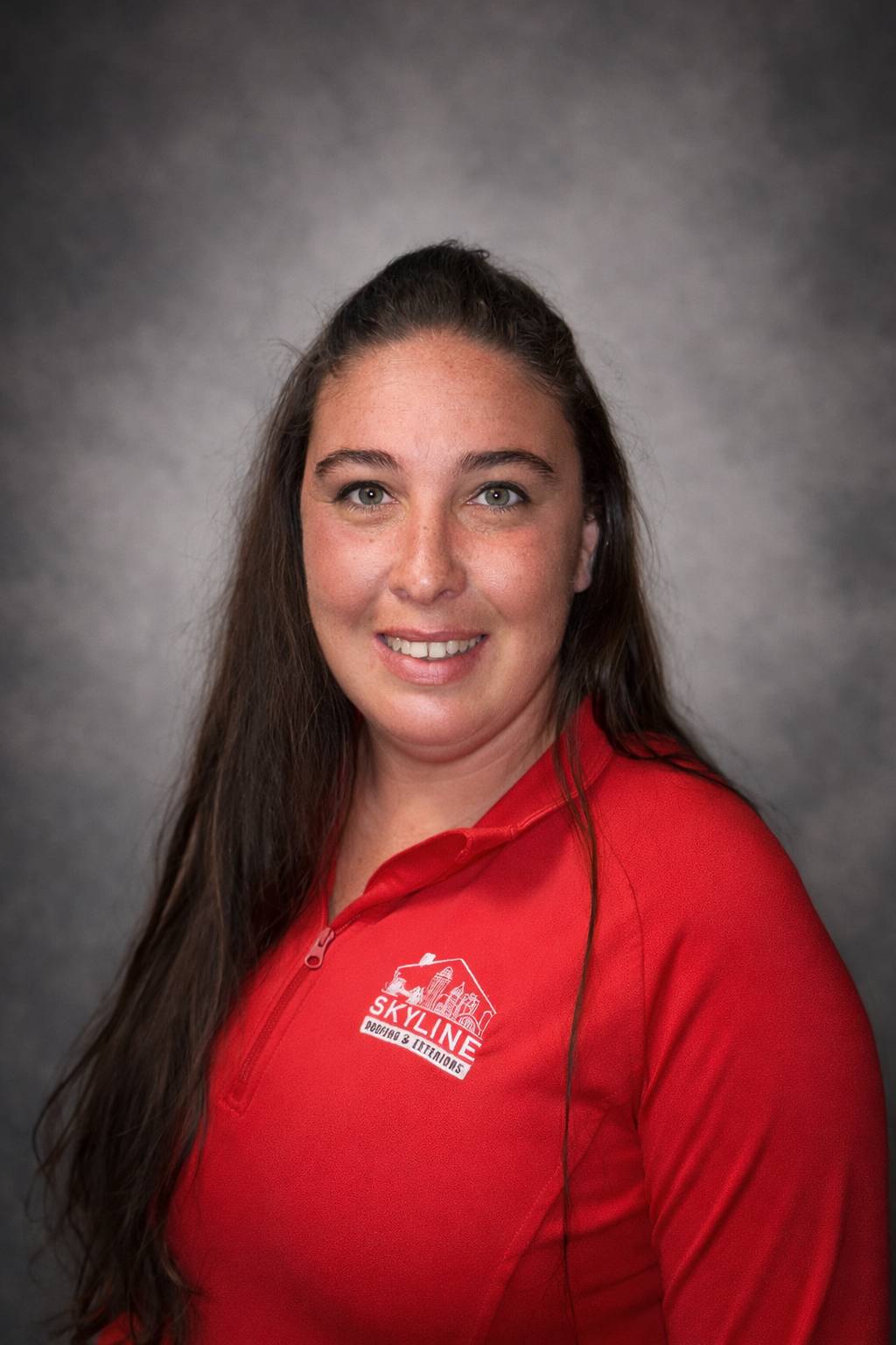 Woman in red shirt smiles at camera. Dark hair, gray background.
