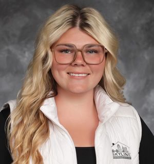 Brandi Carrington. Blonde woman wearing glasses, smiling, and wearing a white vest over a black shirt.