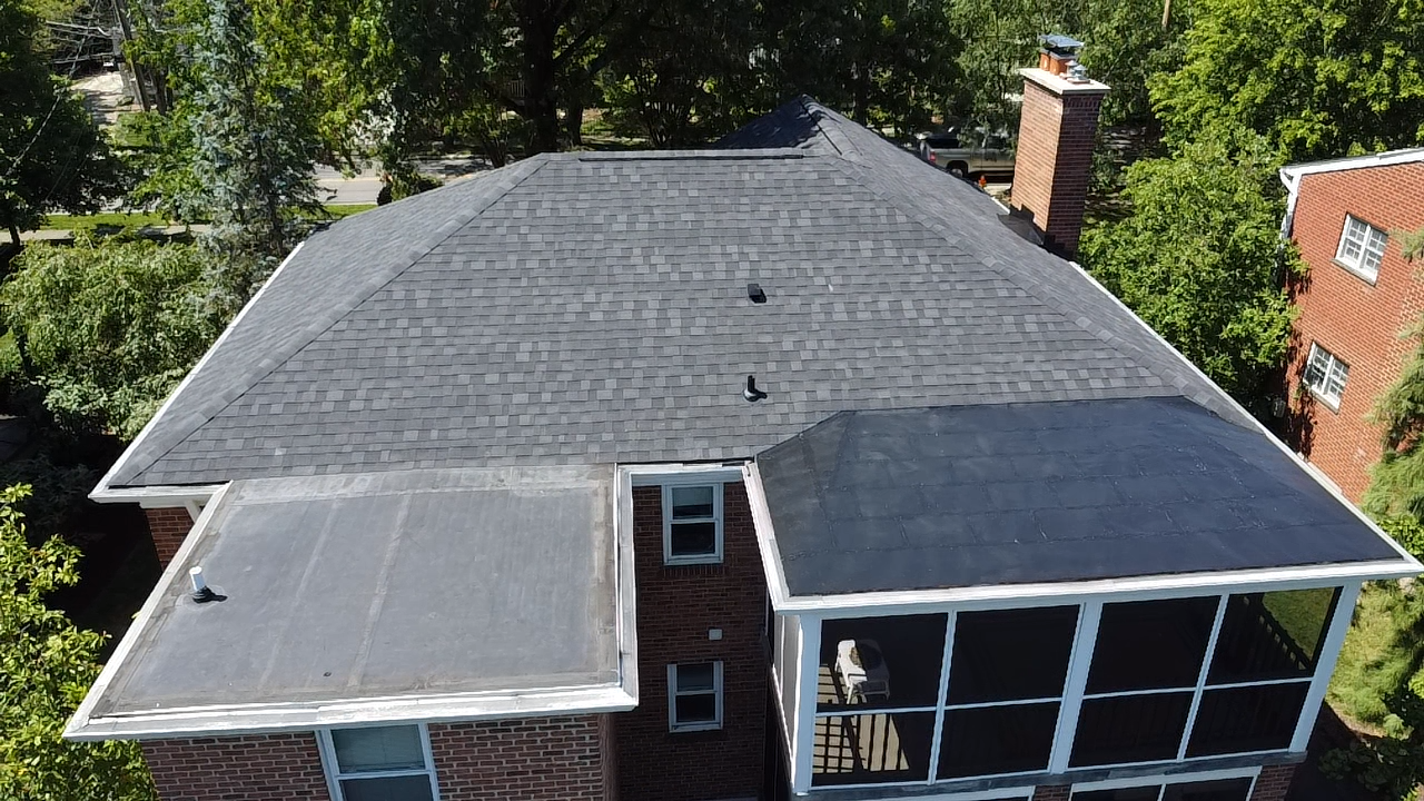 Overhead view of a house with a dark gray shingled roof, brick exterior, and a screened-in porch.