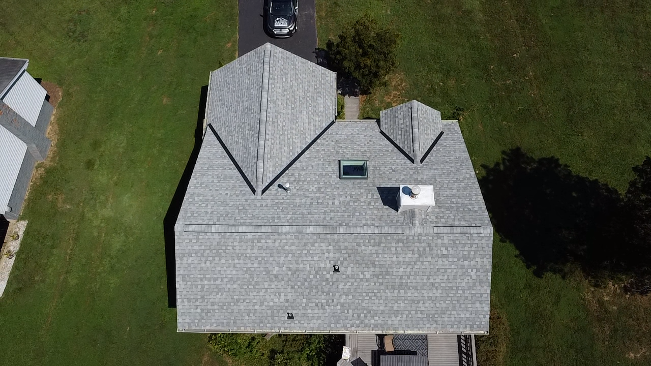 Overhead view of a house with gray roof and a car on the driveway, surrounded by green grass.