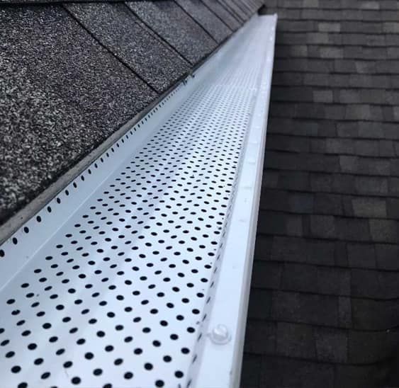 White gutter with perforated cover on a dark shingled roof.