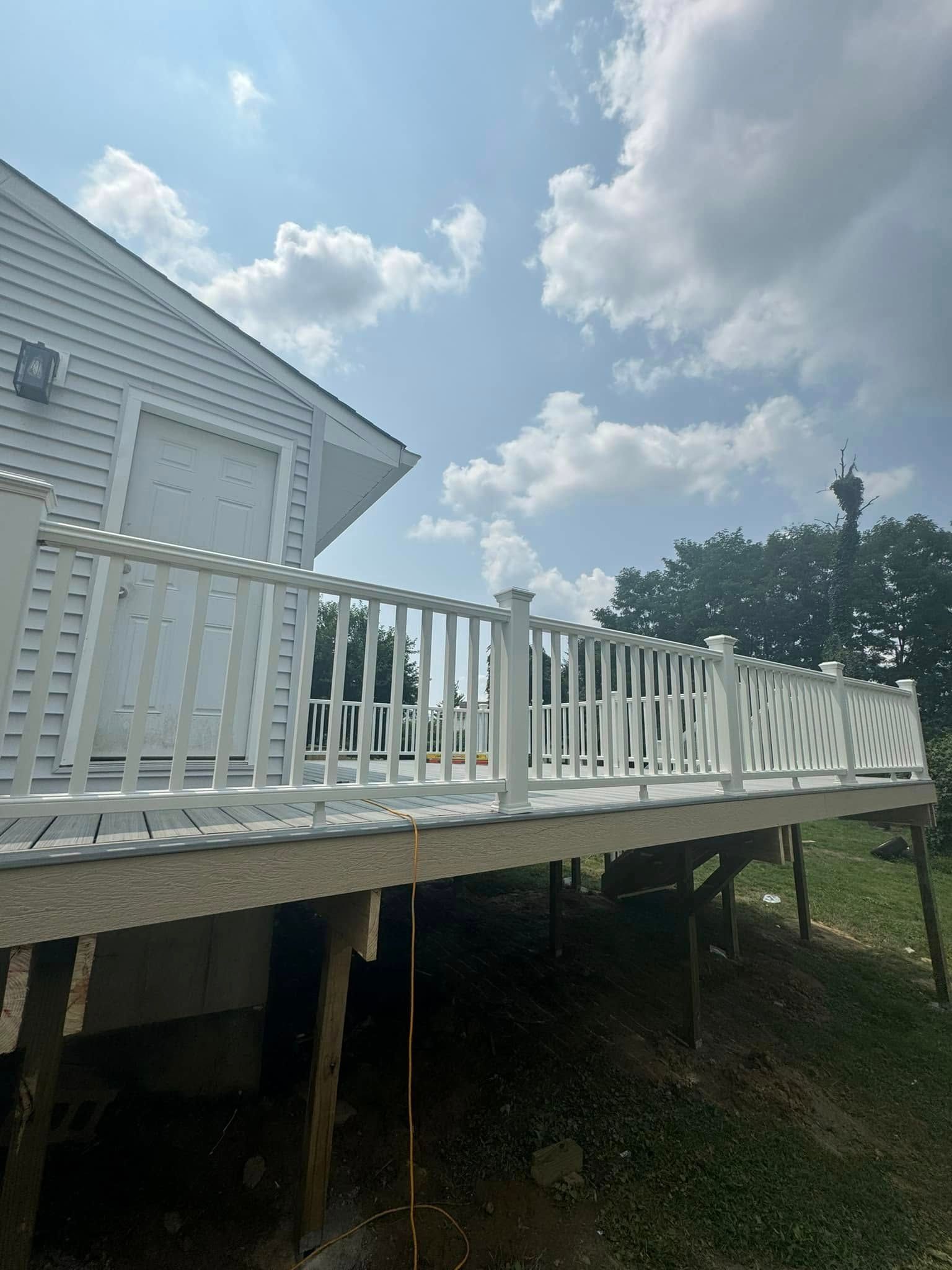 White deck railing on a house, with blue sky and clouds in the background.