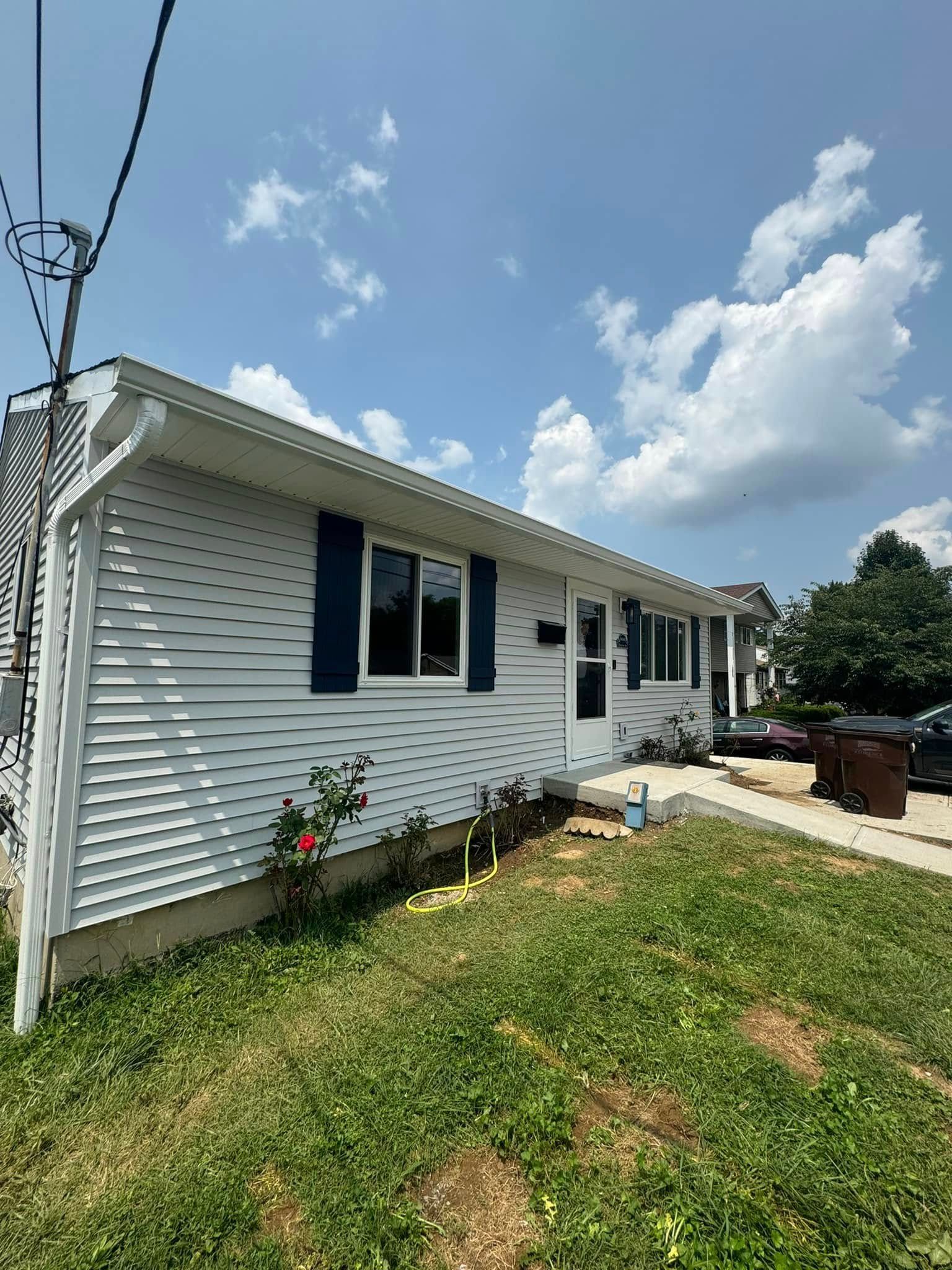 White-sided house with blue shutters and a green lawn under a partly cloudy sky.