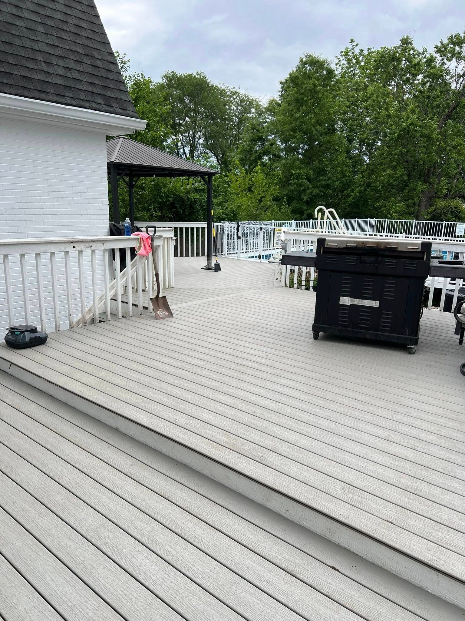 Deck with a grill, surrounded by trees. White railings and a gray deck.