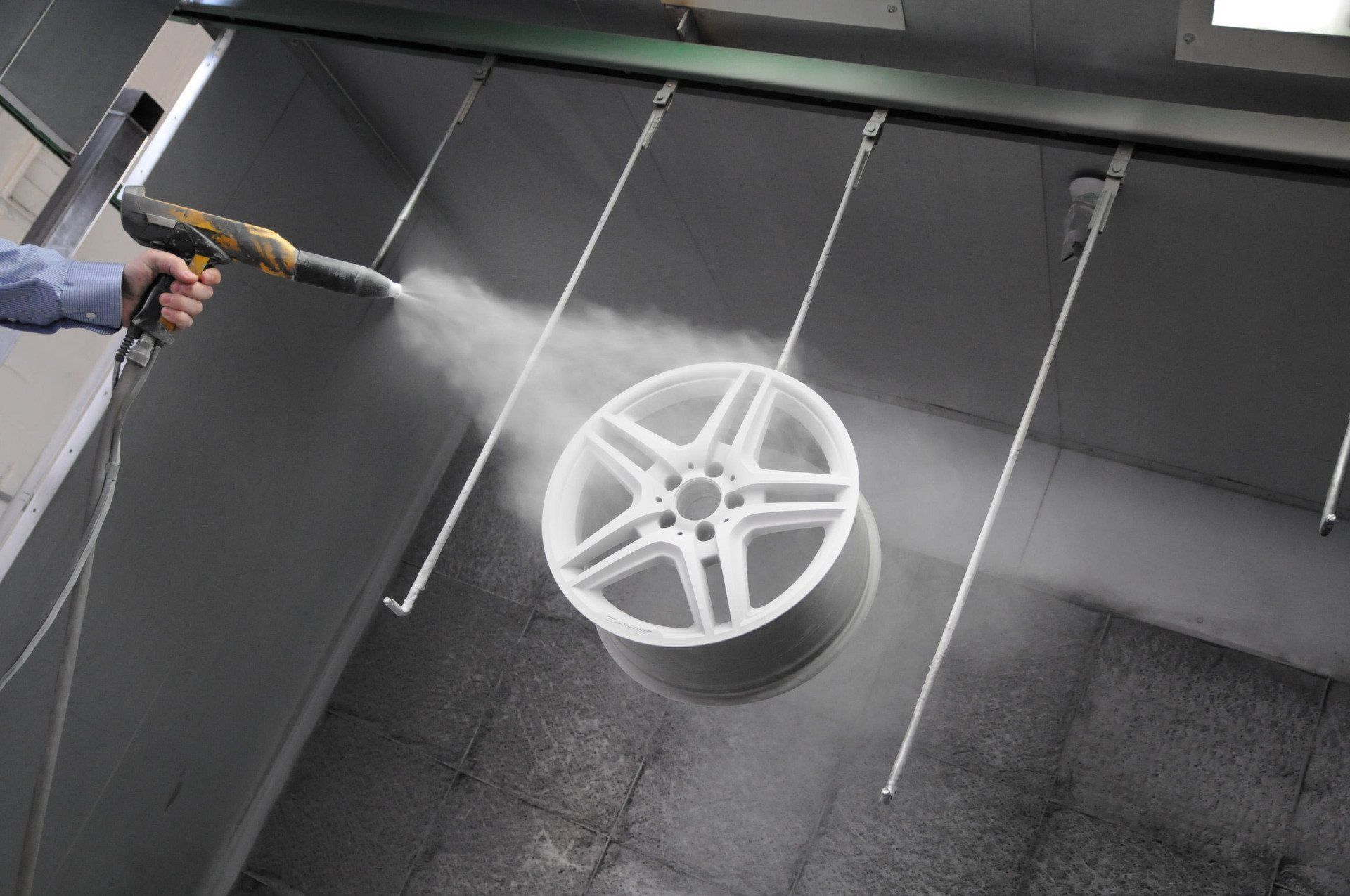 A person spray-painting a white car wheel in a spray booth.