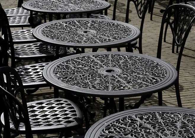 Ornate black metal tables and chairs arranged outdoors on a cobblestone street.