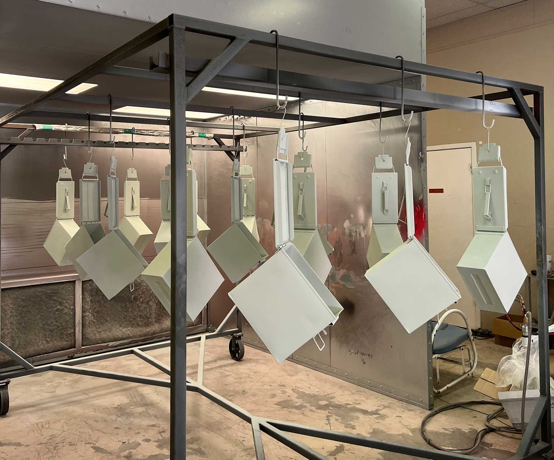 Painted metal boxes hanging on a rack inside a paint booth.
