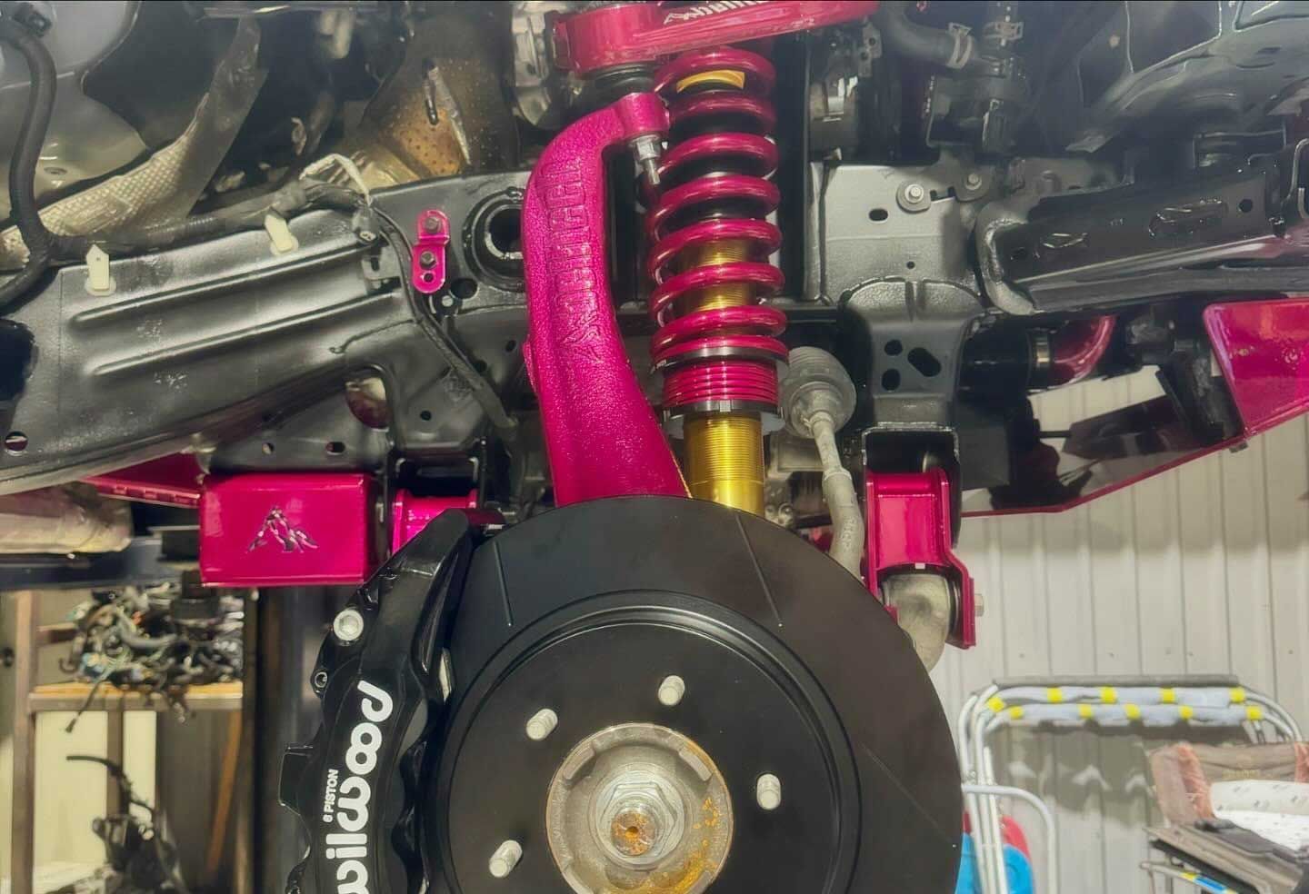 Bright pink modified car suspension components, with a black rotor and gold shock.