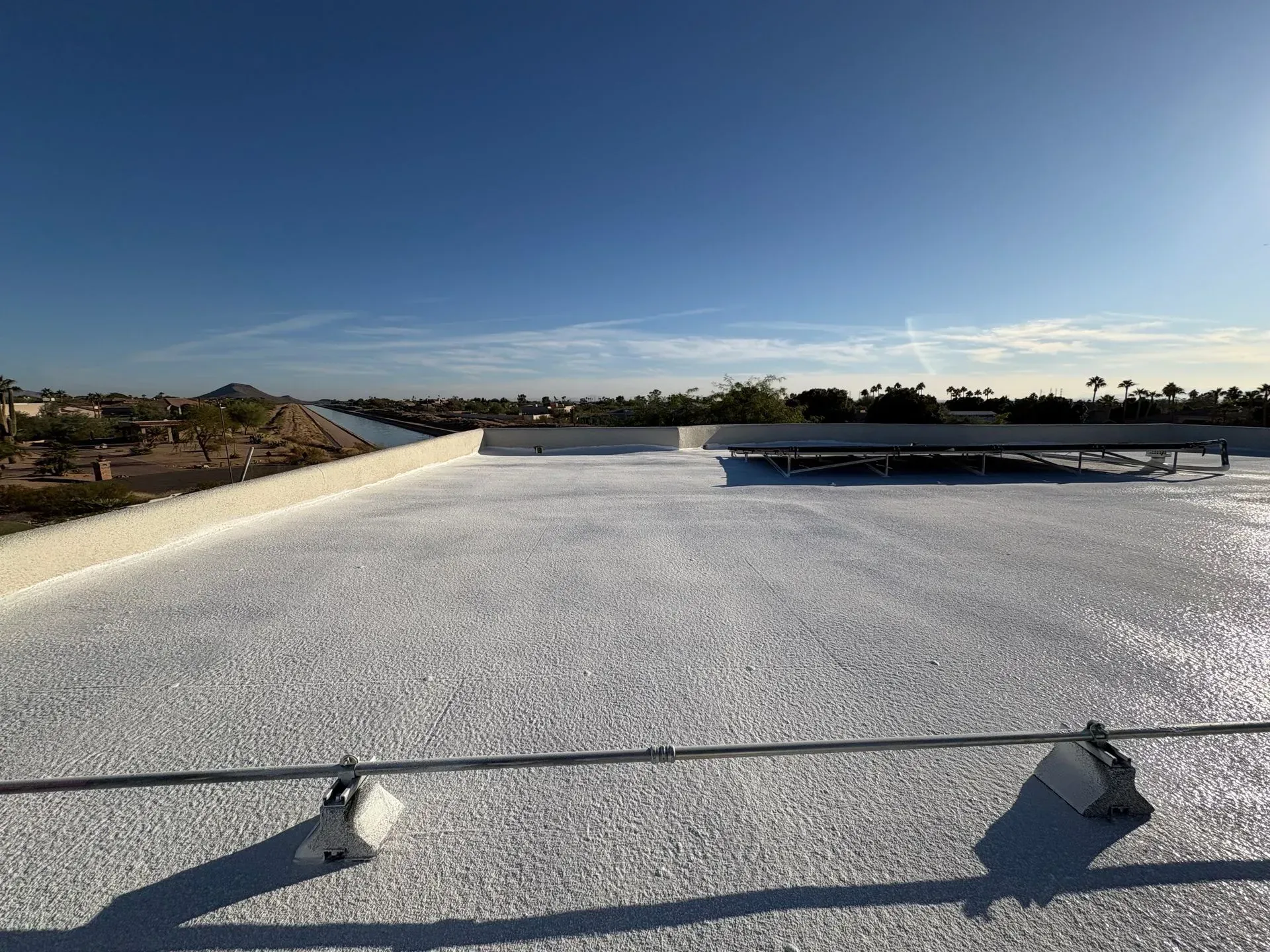 White roof with slight texture under a bright blue sky, with city in the background.