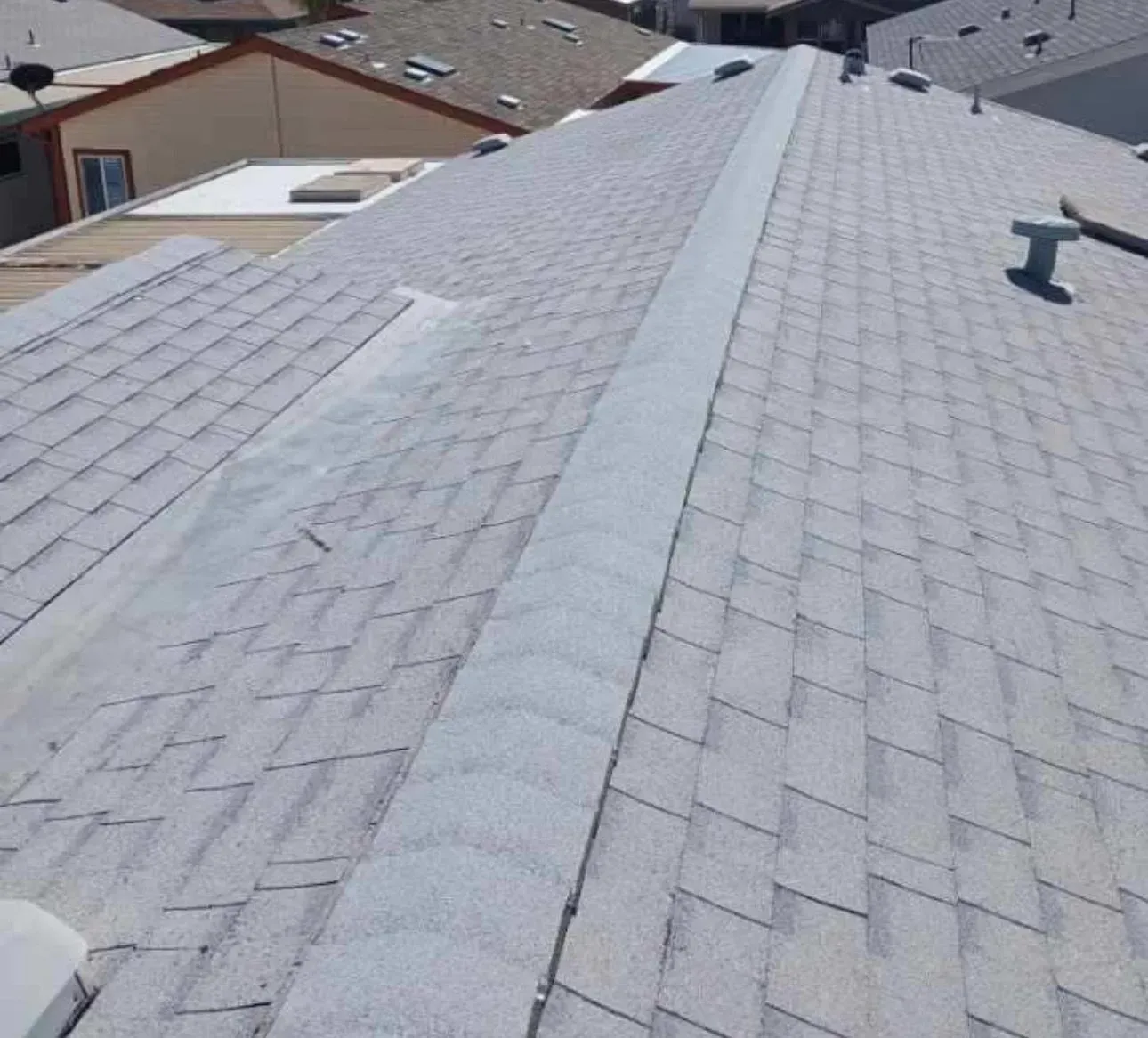 Gray shingle roof with a central flat section and a roof vent, seen from an elevated perspective.