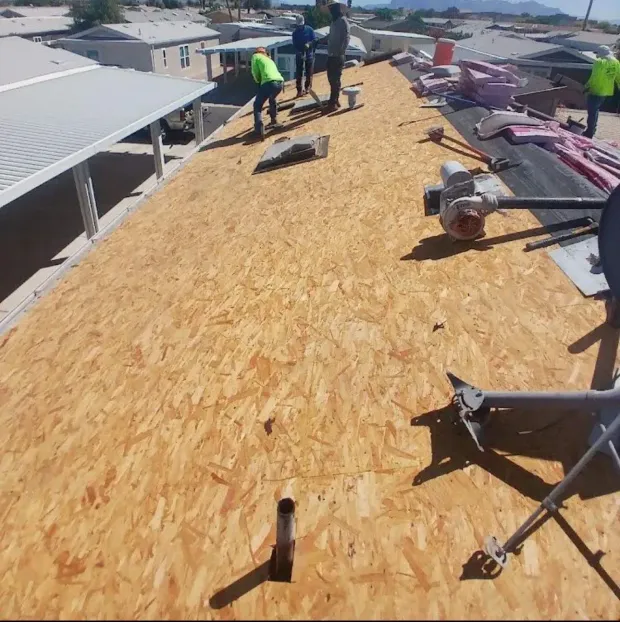 Workers on a roof installing shingles. One worker is wearing a yellow safety vest. The setting is outdoors.
