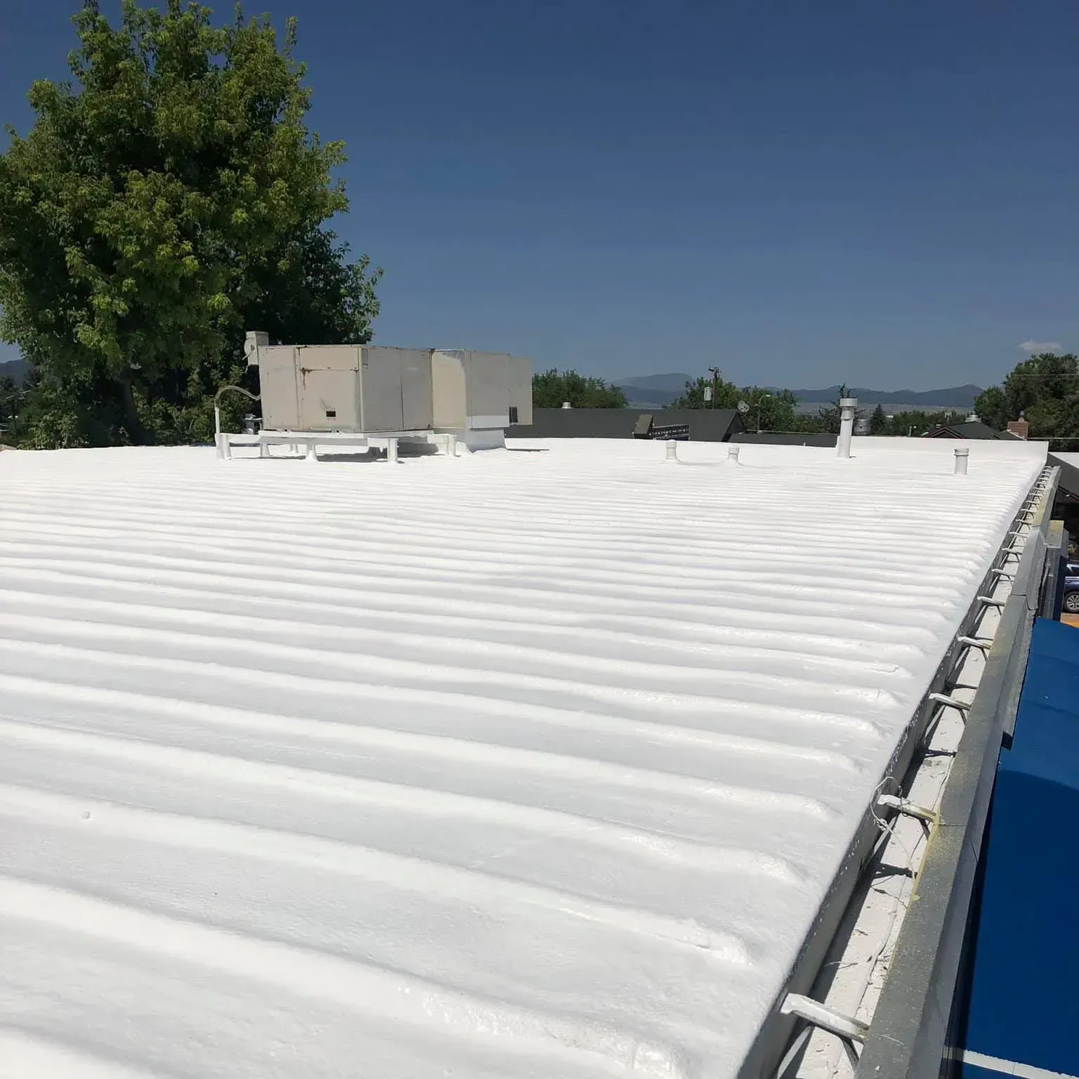 White-coated corrugated metal roof on a building, under a blue sky, with some equipment visible.