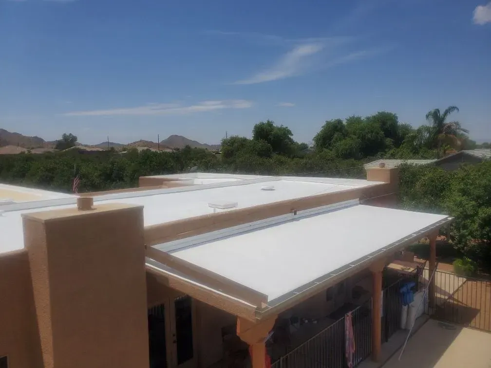 Tan building with a white roof under a blue sky, trees in the background.