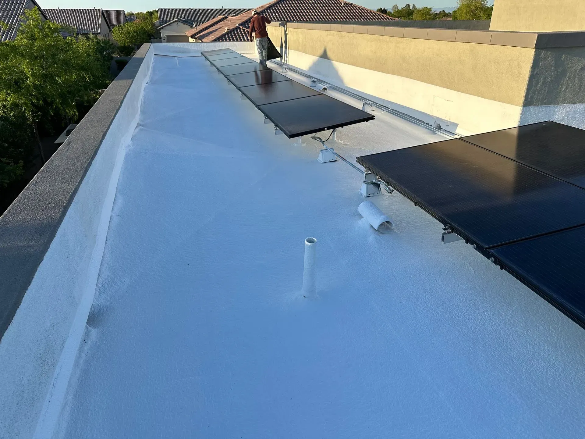 White flat roof with solar panels; someone works near them in the sun.