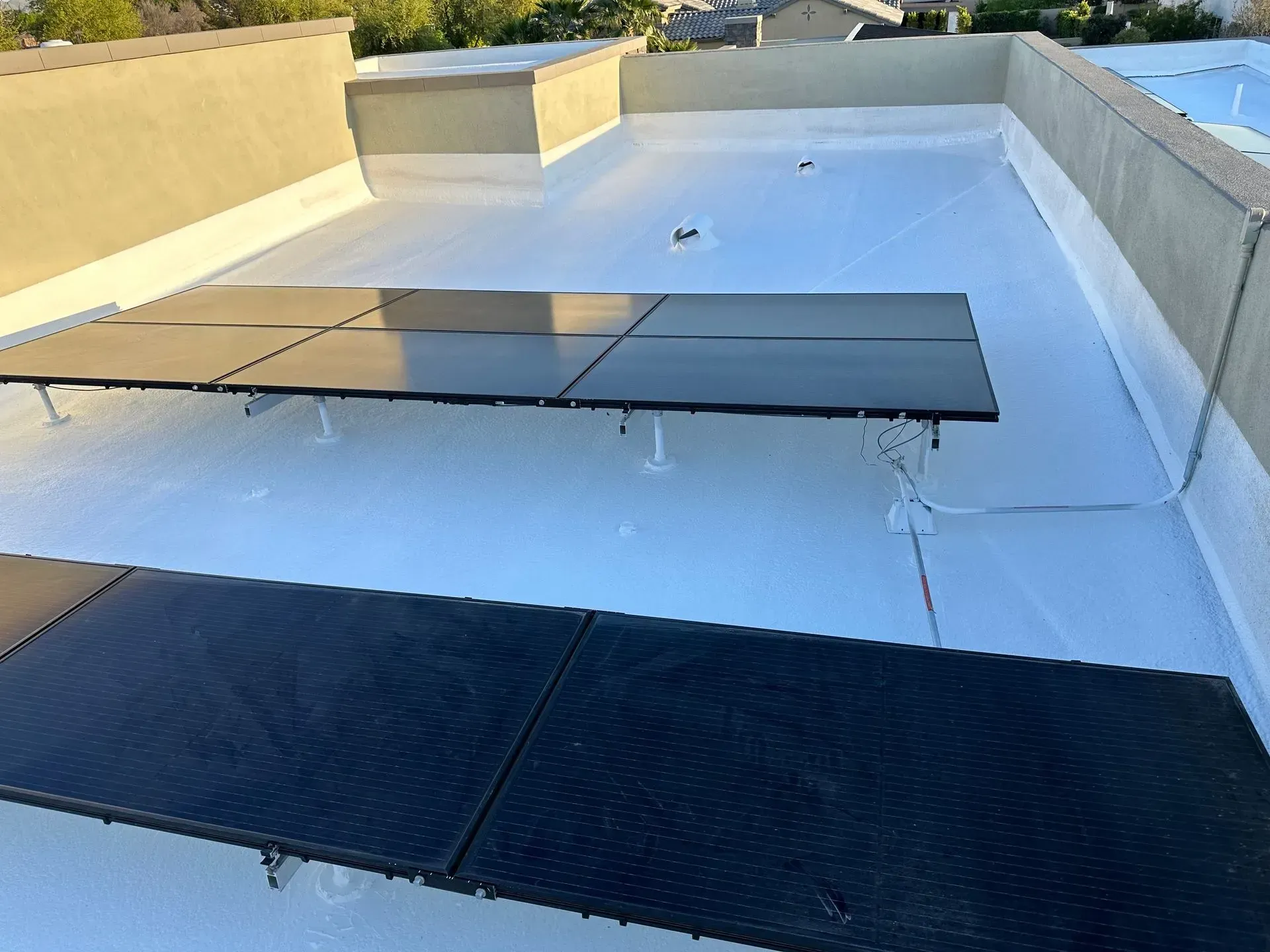 Solar panels on a flat white roof against a building's beige exterior. Wires and brackets are visible.