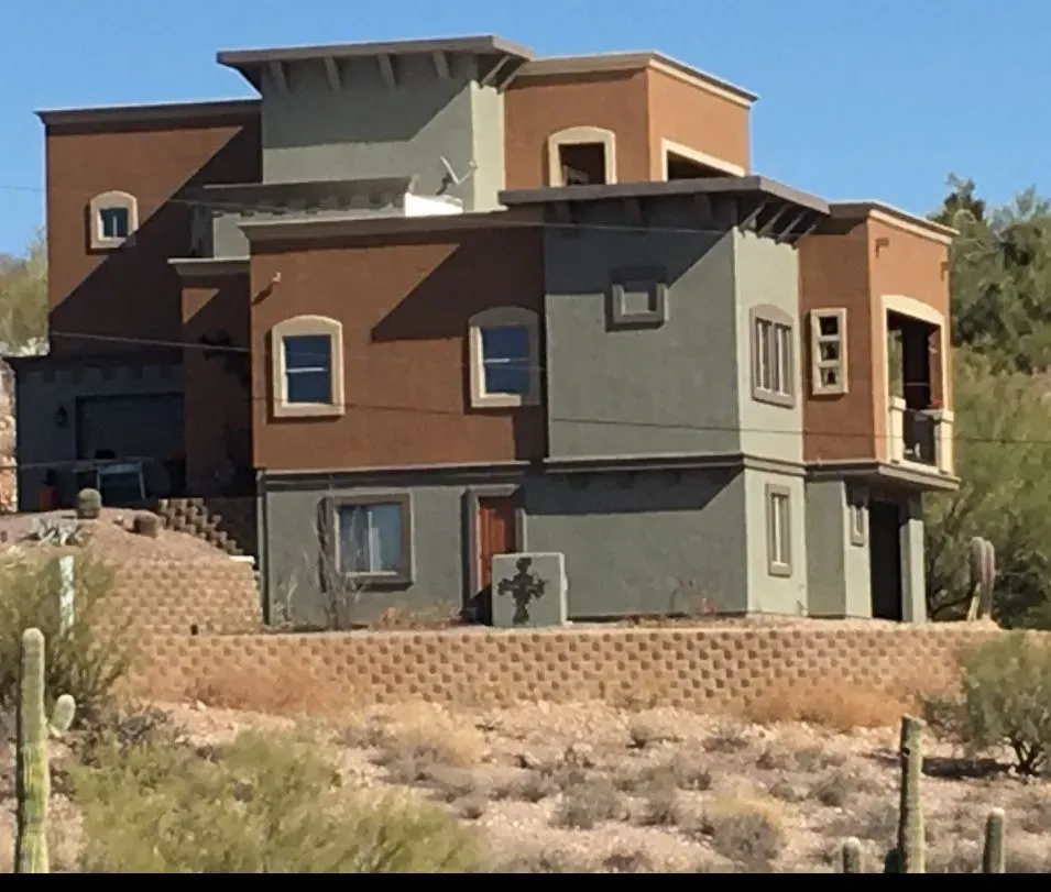 Multi-story stucco house in desert setting; brown and green exterior; terraced landscaping.