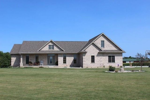 Single-story stone house with a large front porch and expansive green lawn under a blue sky