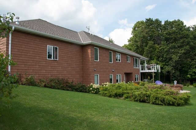 Brick apartment building with white-trim windows, green lawn, and trees under a cloudy sky