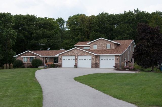 Suburban brick house with three-car garage and curved driveway, surrounded by a green lawn and trees