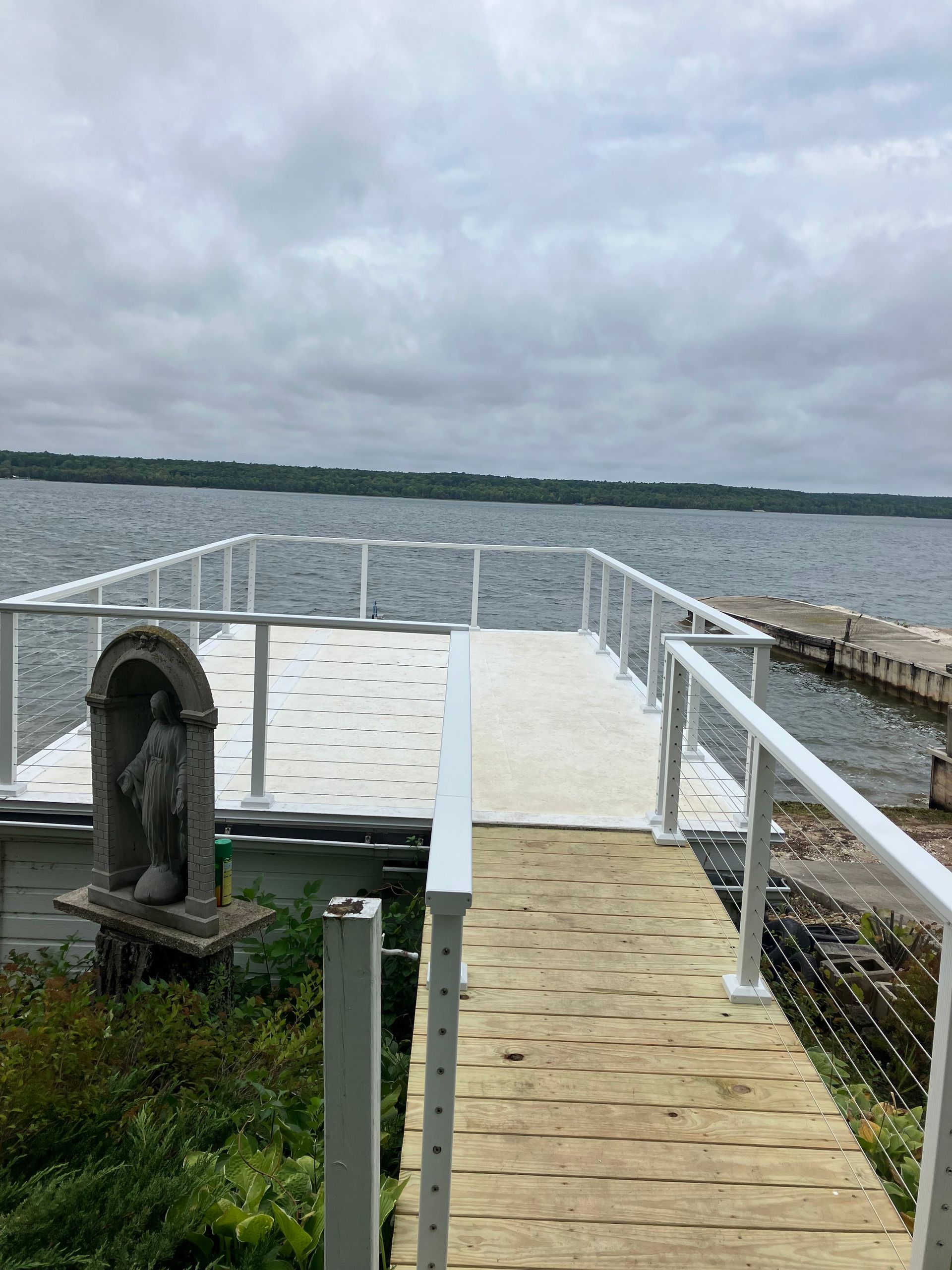 Pier overlooking a cloudy lake, with white railings and a small statue in the foreground