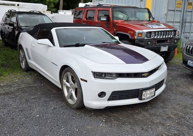 White convertible car with purple stripe parked next to a red Hummer in a gravel lot.