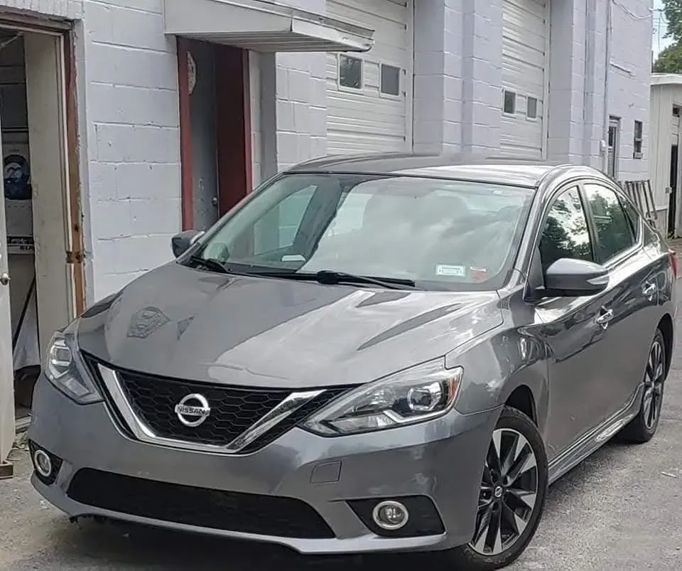 Gray Nissan Sentra sedan parked in front of a building with garage doors; sunny day.